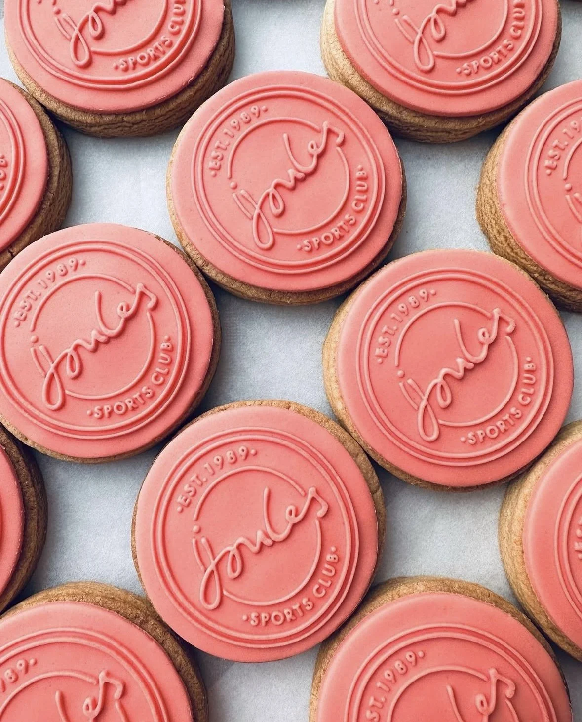 Several round cookies with pink icing on top, featuring a logo that reads 'Joma Sports Club' with the establishment year '1969' embossed around the circle.