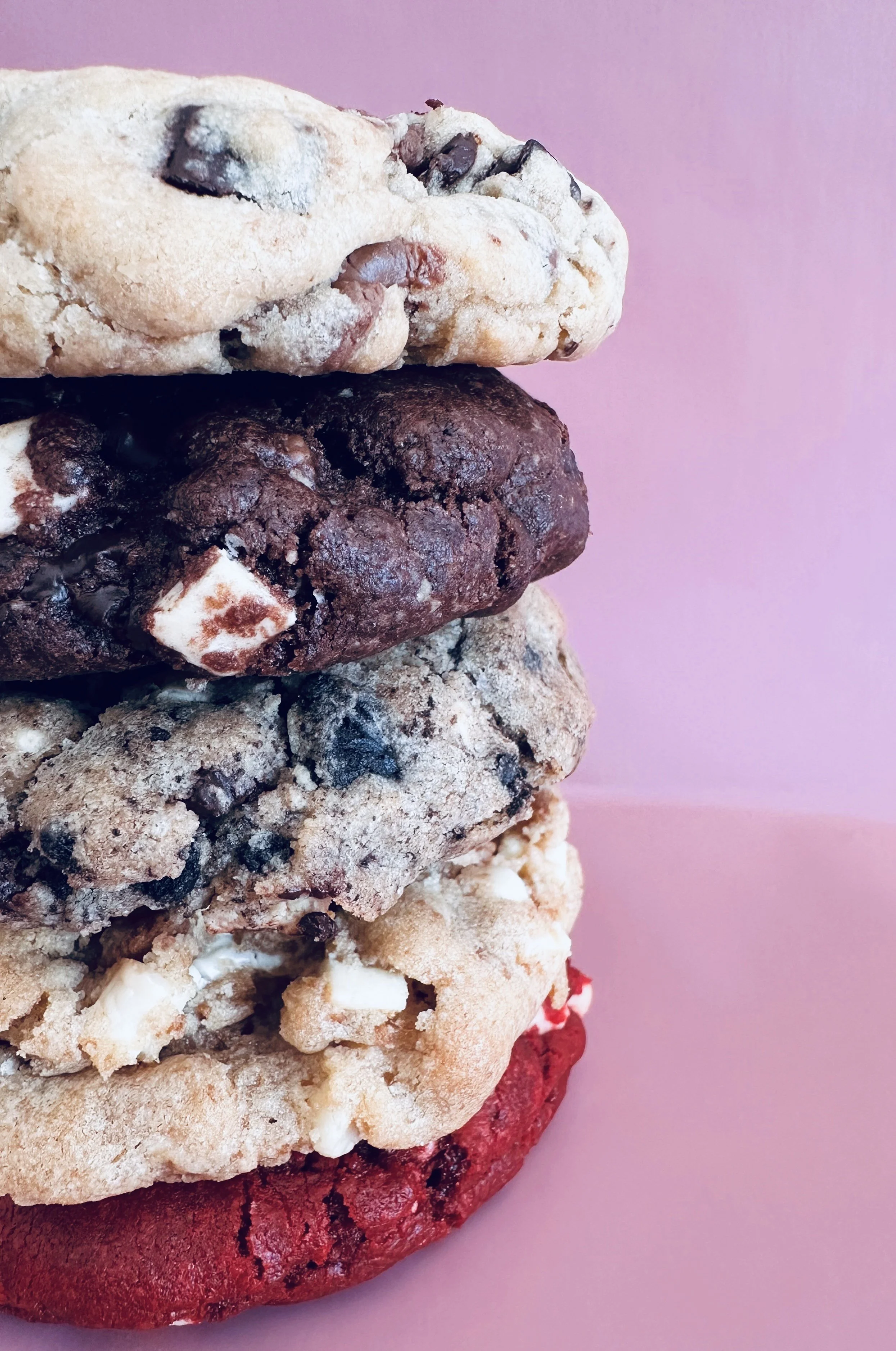 Close-up of a stack of different flavored cookies against a pink background.