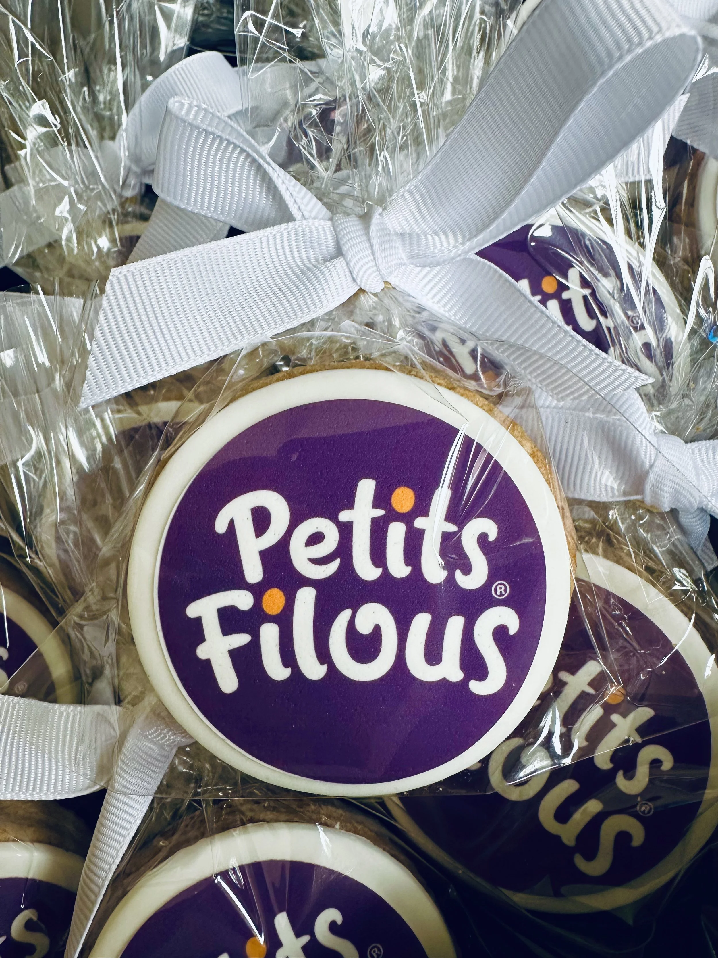 Close-up of Petits Fleurs cookies wrapped in clear plastic with white ribbons.