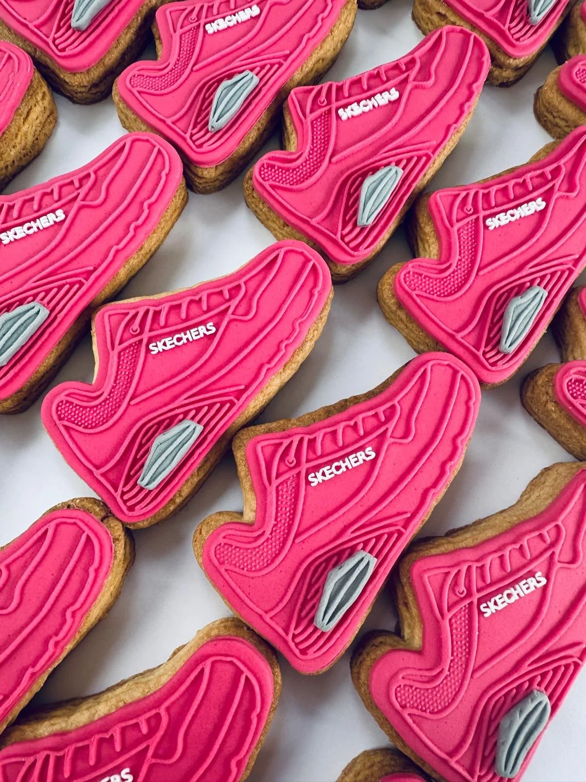Cookies decorated with pink icing shaped like Skechers athletic shoes, with detailed lines and the Skechers logo in white.