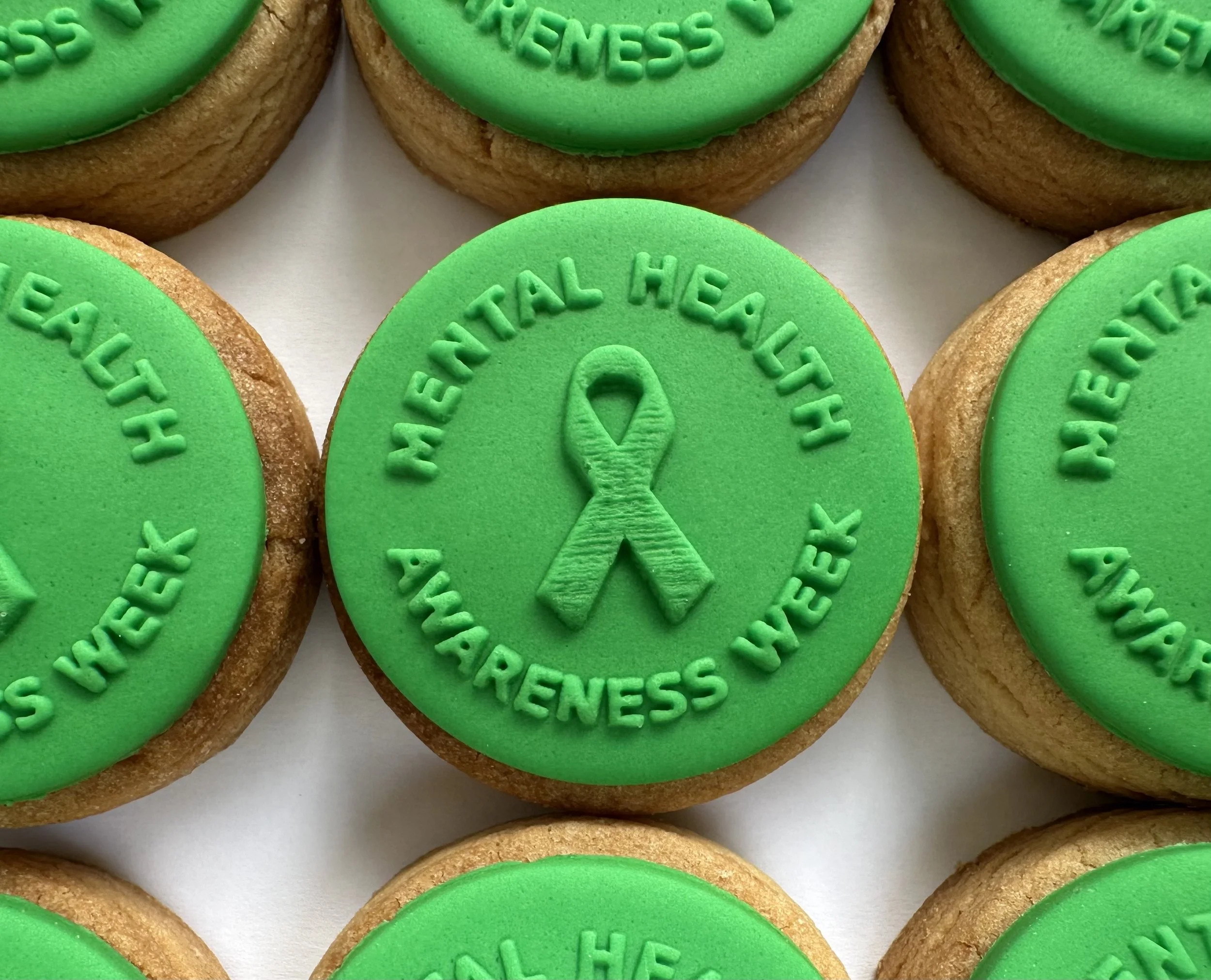 Close-up of green circle cookies with safety message and ribbon design, arranged on a white surface.