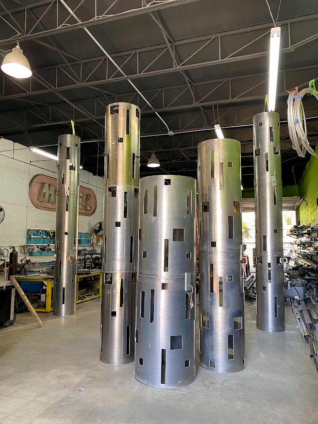 Five large cylindrically-shaped metal structures with rectangular and vertical cutouts in a workshop or industrial setting.