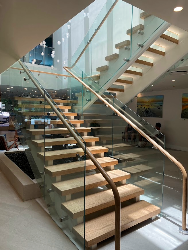 Wooden stairs with glass sides and a wooden handrail in a modern building lobby.