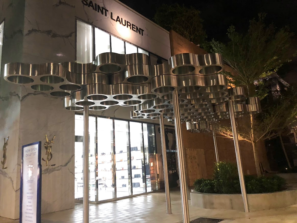 Night view of Saint Laurent store entrance with metallic cloud-like canopy and glass doors, with trees and lit signage.