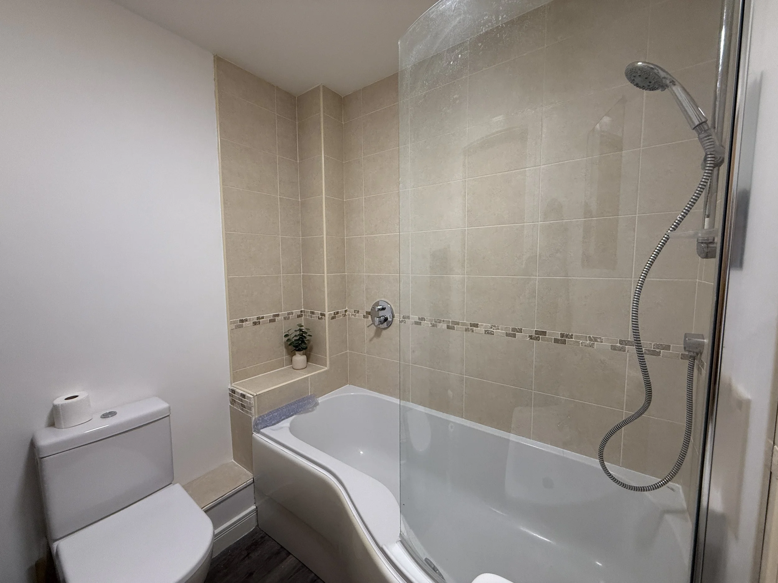 Bathroom with white toilet, bathtub, beige tiled wall with decorative border, and shower head with hose.