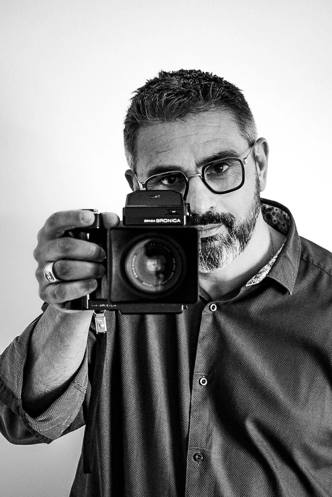 Homme avec lunettes prenant une photo avec un appareil photo. Éclairage uniforme, fond clair.