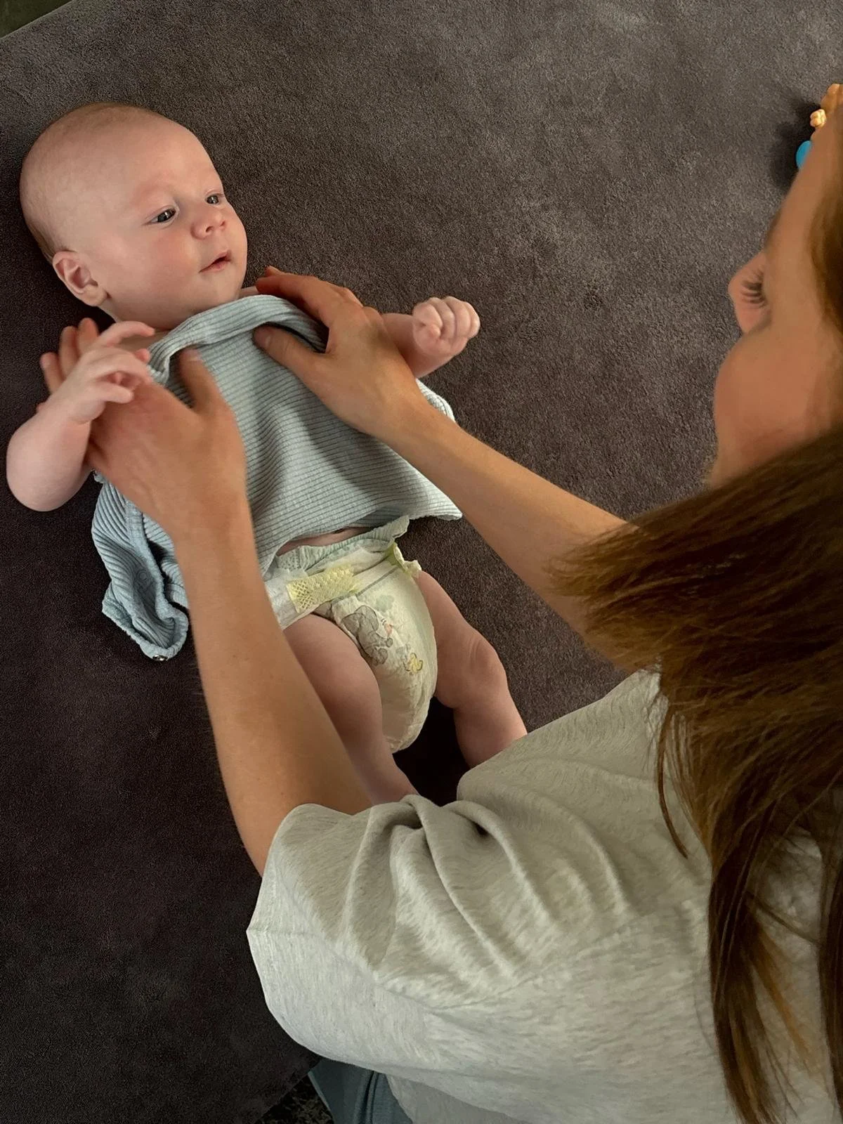 Een baby ligt op de grond, terwijl een vrouw hem vasthoudt en naar hem kijkt.