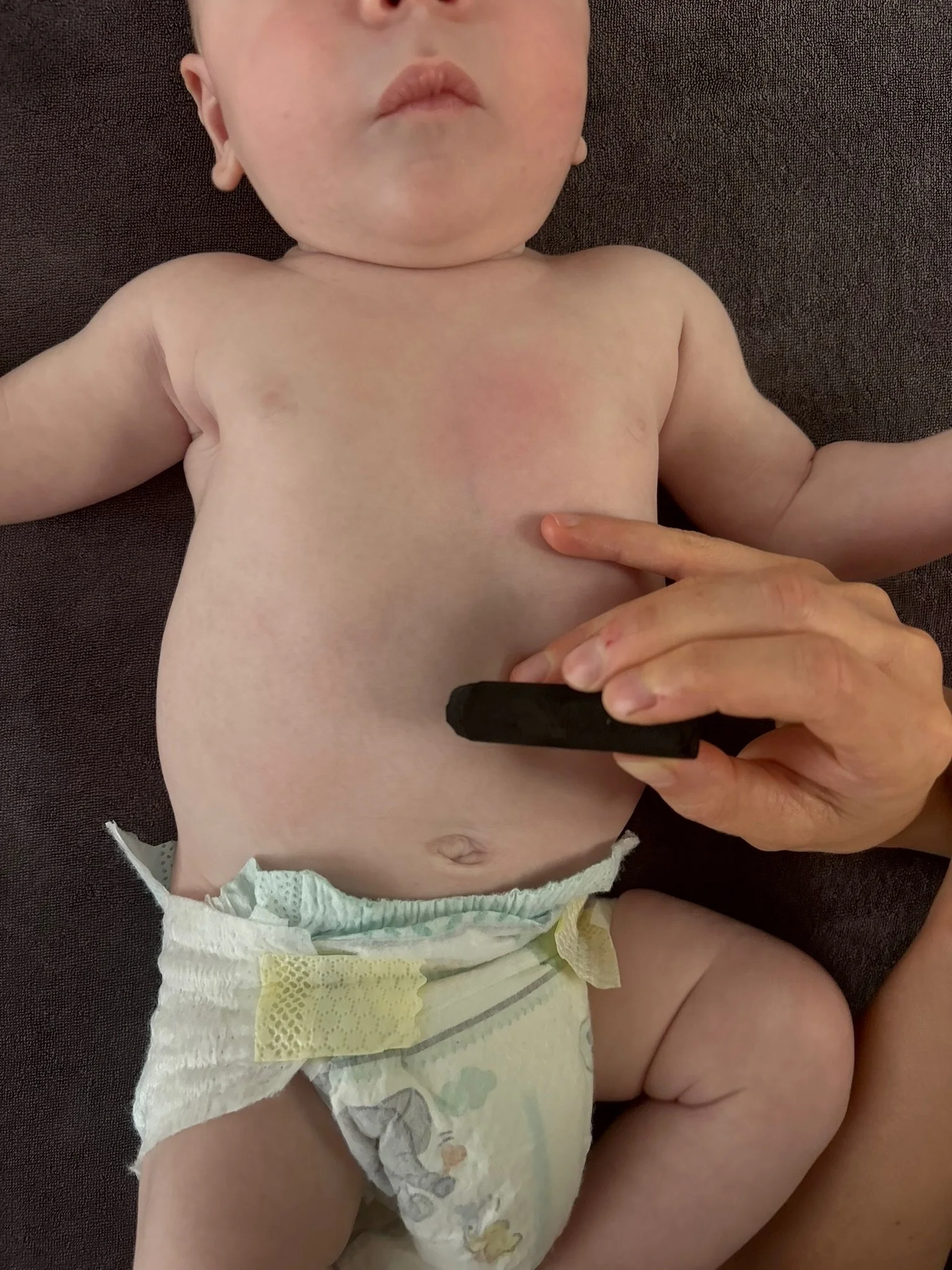 Een baby ligt op een donkere bank, wordt verzorgd door een persoon met Moxa.