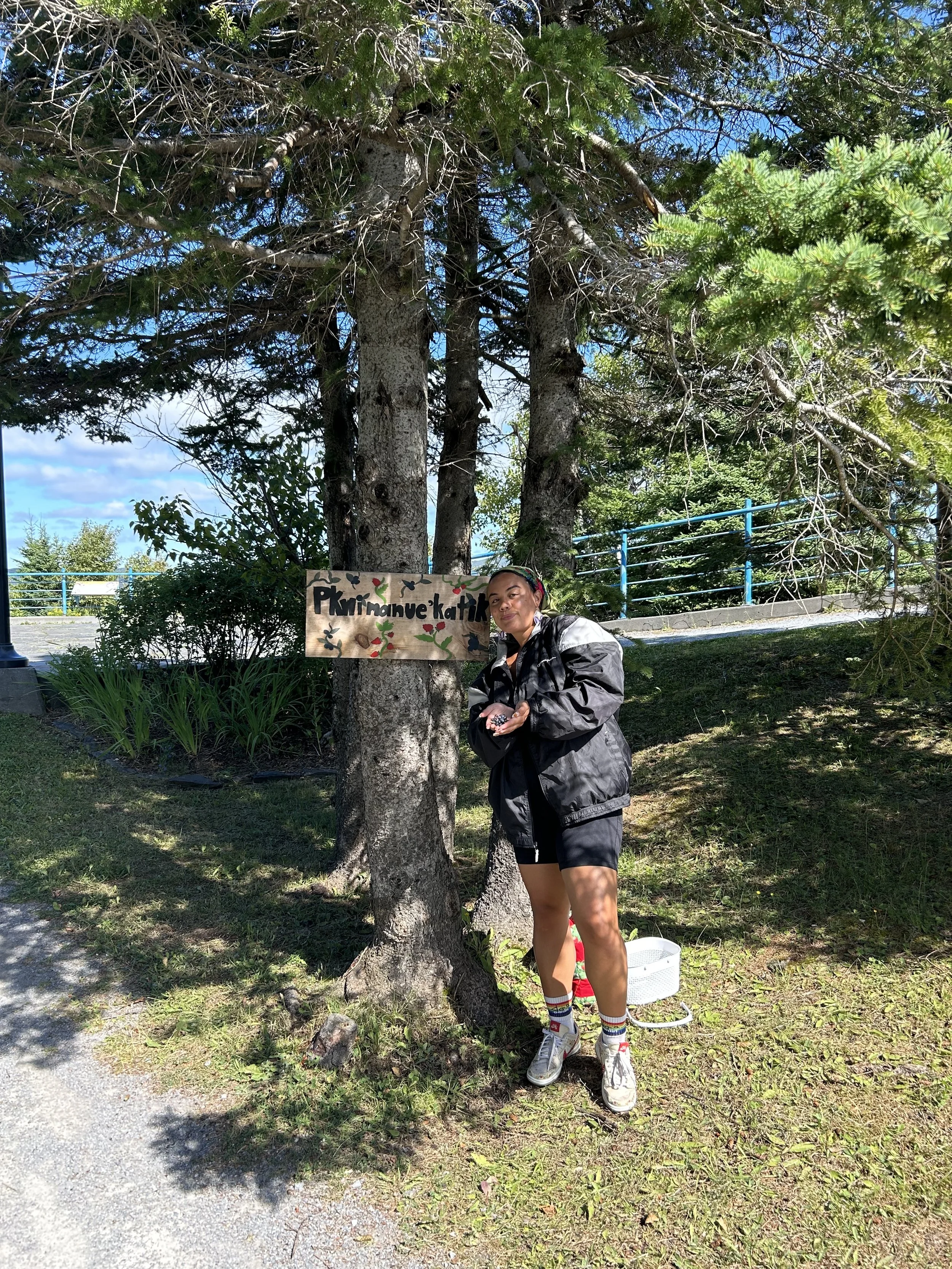 Kaitlin standing with Pkwimanue’katik sign,  meaning the "place where the blueberries are plenty" in Mi'kmaw.