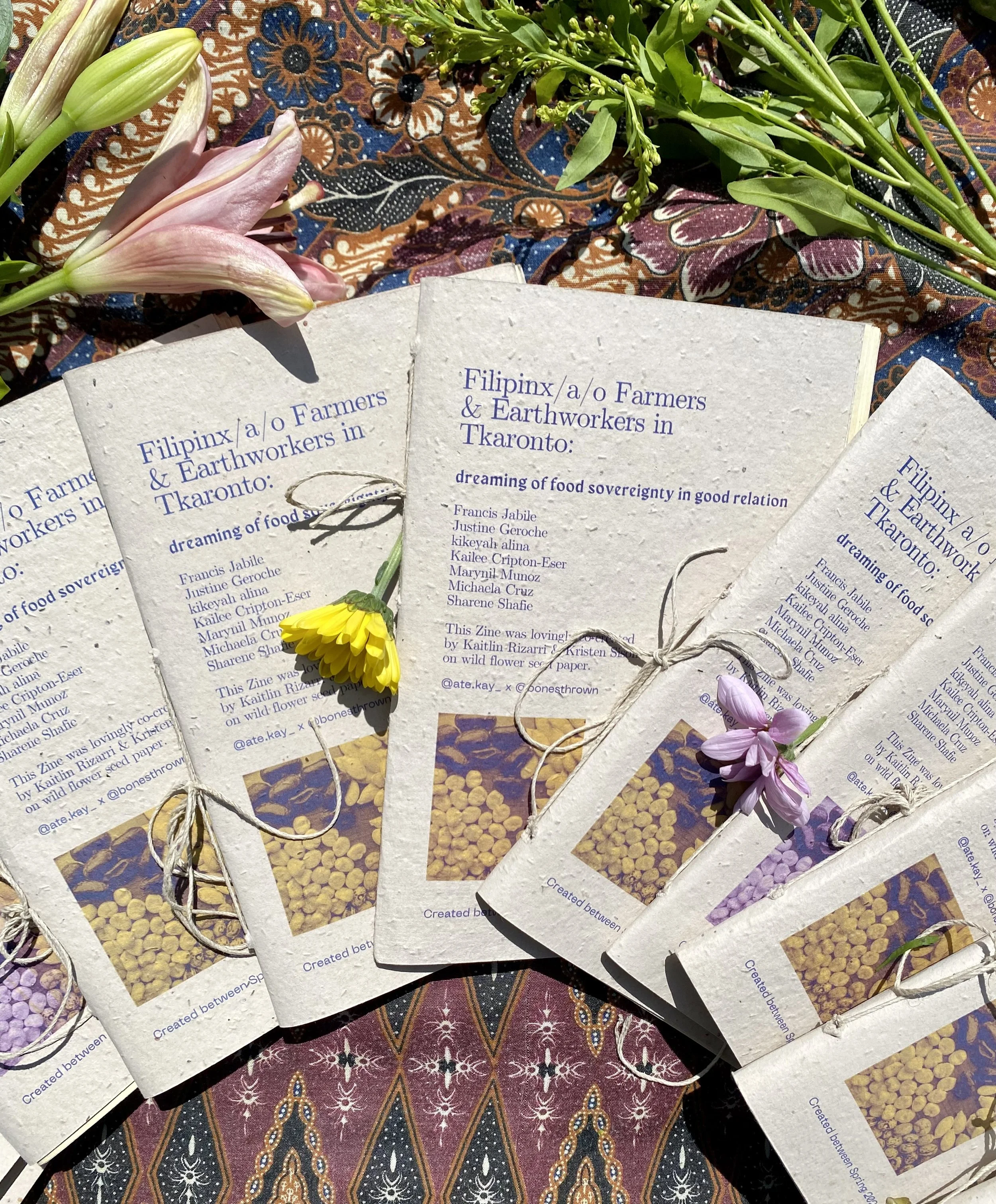 Filipino Food Sovereignty Zine that interviewed Filipino farmers in Toronto. Several printed zines with text and images on a colorful fabric surface, surrounded by flowers and greenery.