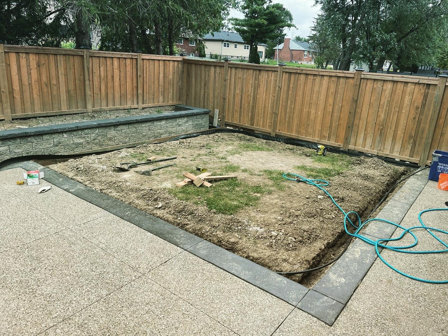 Backyard with a construction project underway, featuring soil excavation, a wooden fence, and construction tools.