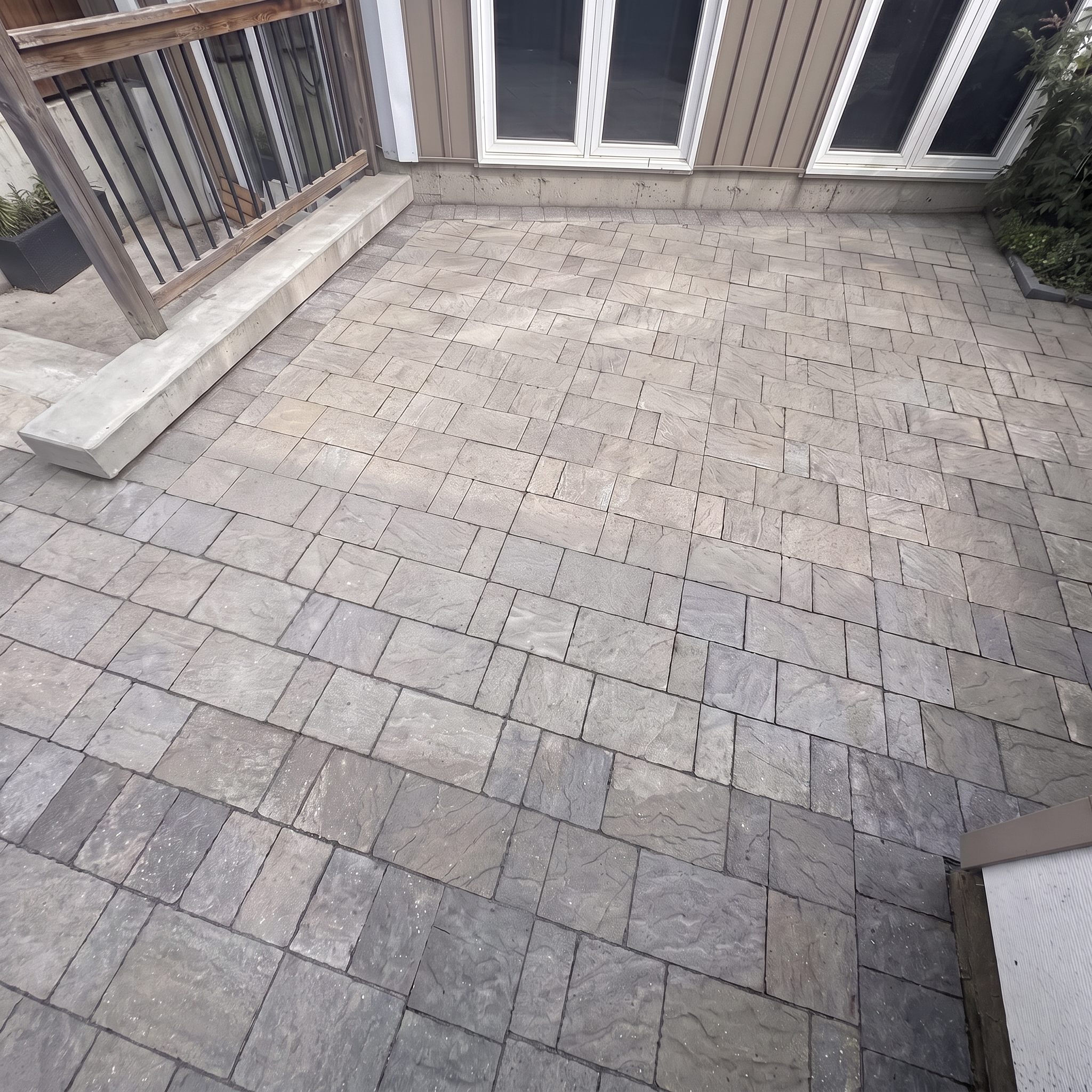 An outdoor patio with stone tiles, a wooden railing, a sliding glass door, and some plants on the side.
