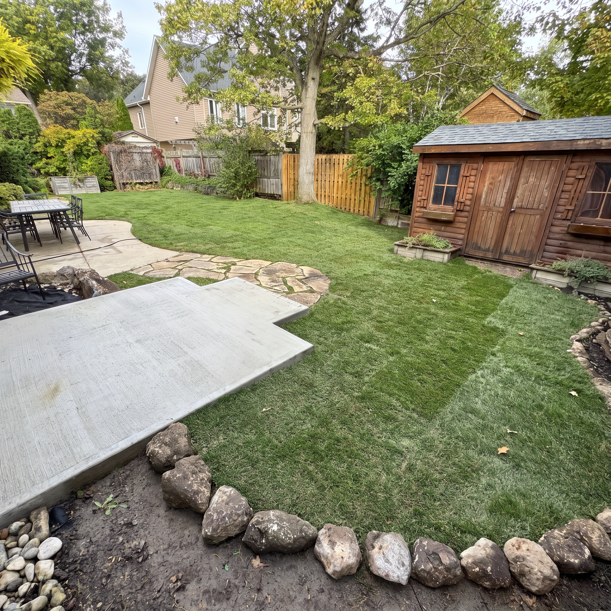 Backyard with a concrete patio, a grassy area, a large tree, a wooden fence, a small shed, and outdoor seating.