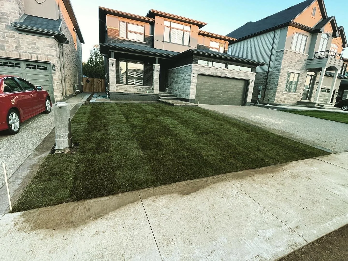 Freshly laid sod grass in front yard of modern house with brick and stone exterior, driveway, and neighboring houses.