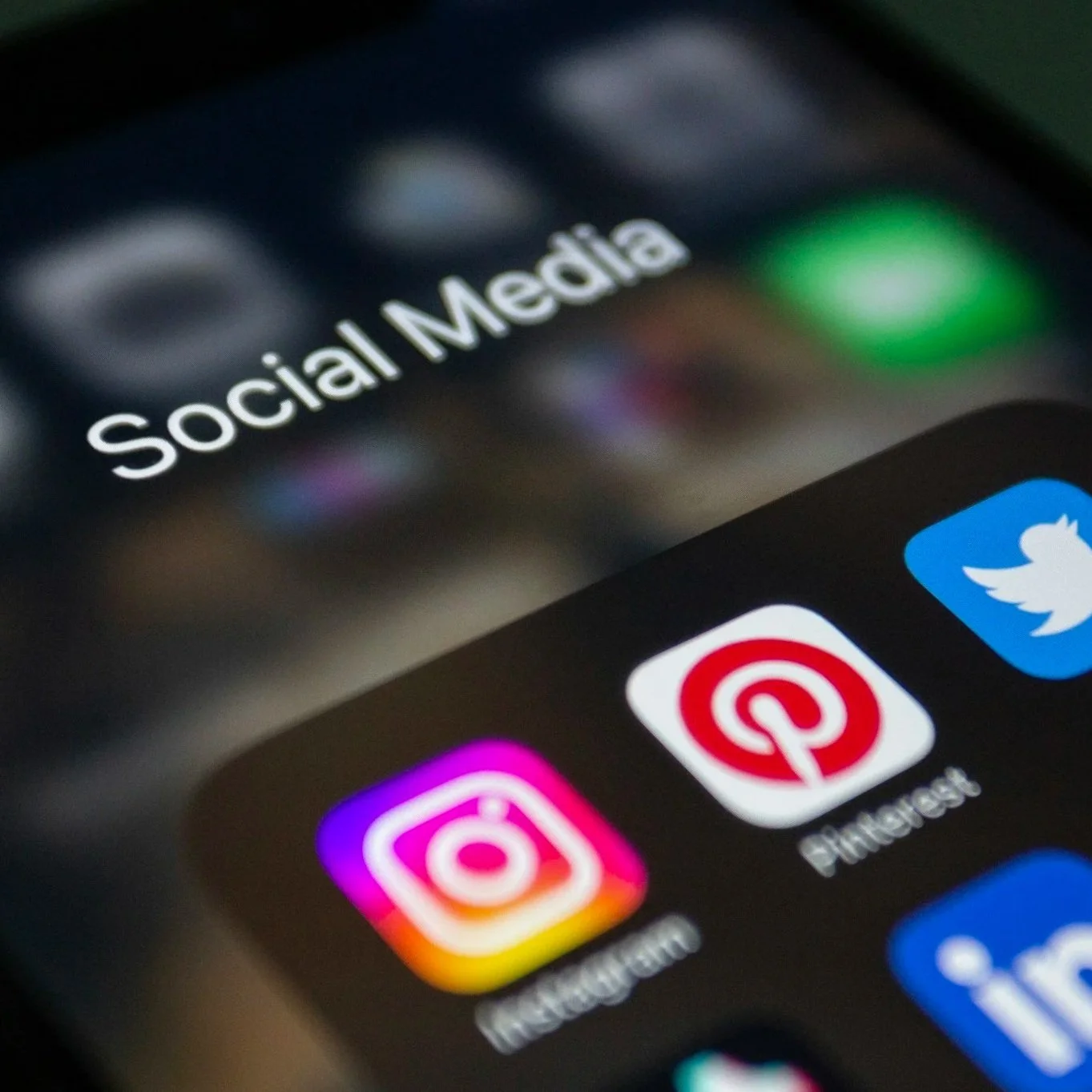 Close-up of a smartphone screen displaying the social media folder with icons for Instagram, Pinterest, Twitter, and other apps.