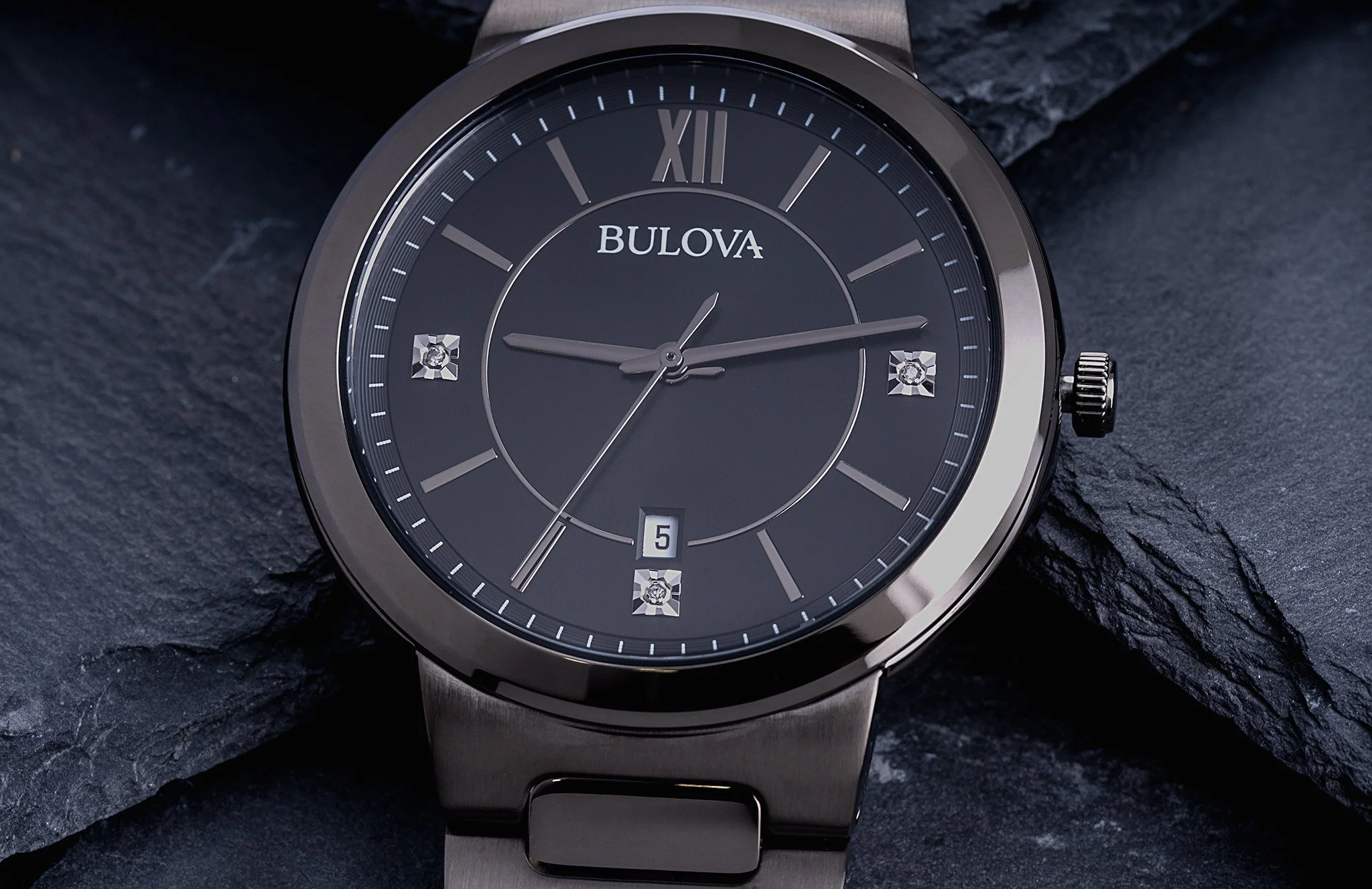 A Bulova wristwatch with a black dial, silver and diamond accents, and a date display, resting on a dark textured surface.