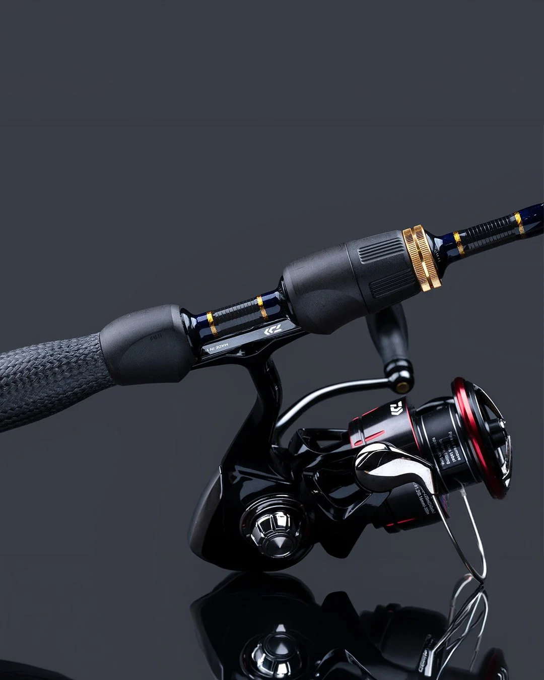 Close-up of a black fishing reel attached to a fishing rod on a reflective dark surface.