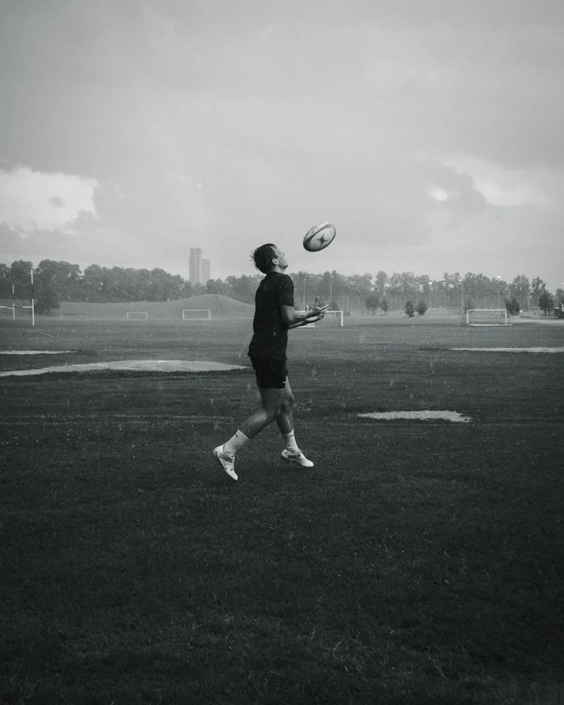 Junge spielt  Rugby auf einem leeren Sportplatz, läuft und fängt den Ball in der Luft.