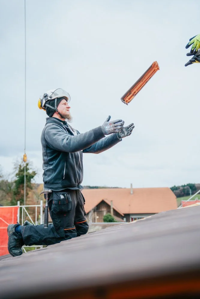 Der Arbeiter wirft ein Ziegel in die Luft auf einer Baustelle, trägt Sicherheitshandschuhe, Helm und dunkle Arbeitskleidung.