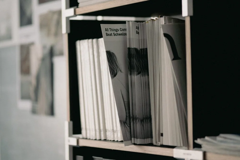 Bilderregal mit Zeitschriften, darunter eine Zeitschrift mit dem Titel 'All Things Considered' und einem schwarzen und weißen Foto einer Frau.