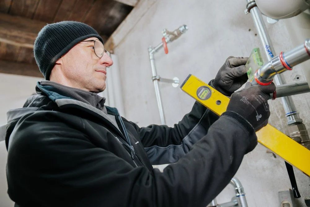 Ein Installateur, prüft die Wasserleitungen mit einem Wasserwaage-Werkzeug in einem Kellerraum.