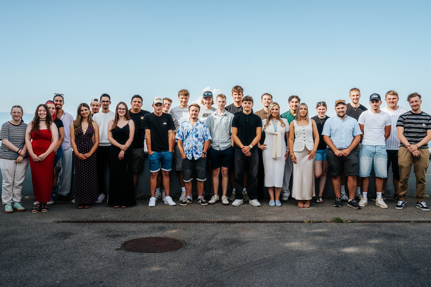 Gruppe junger Menschen im Freien, vor einem blauen Himmel, posieren für Foto.