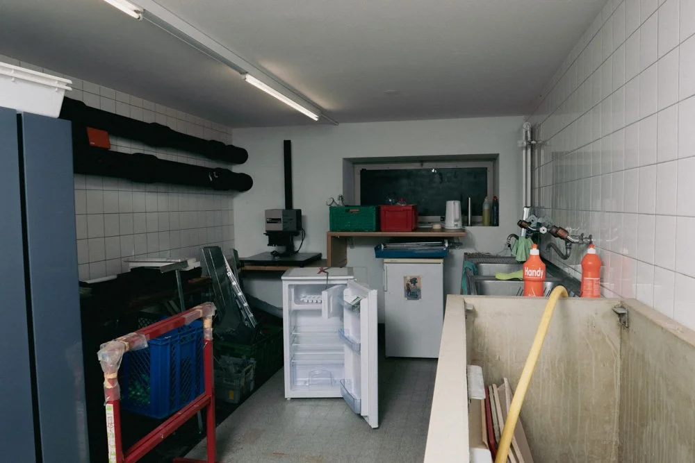 Ein Geschirrspüler steht in einem Waschraum mit Reinigungsmitteln, Werkzeugen und Utensilien auf einem Holzregal