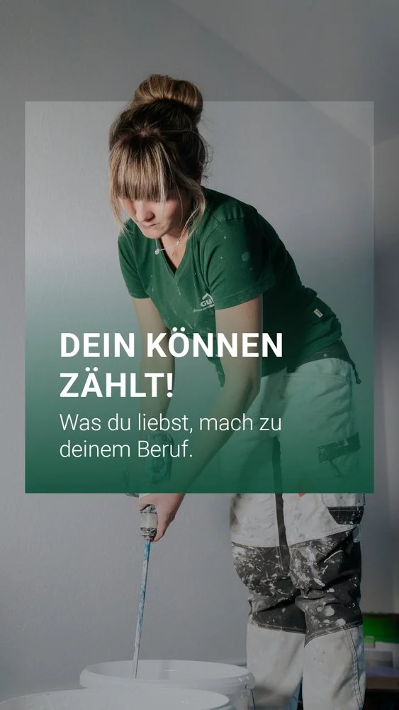 Frau in grünem T-Shirt streicht eine weiße Wand, während sie an einem Farbtopf steht.