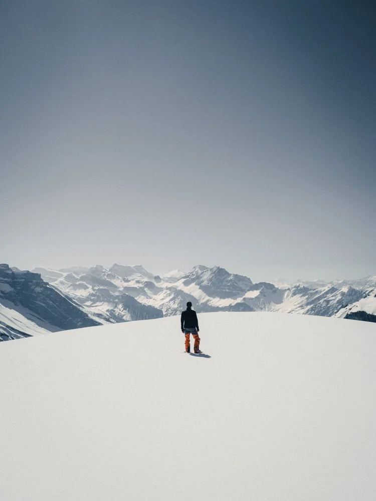Ein Mensch steht in Schnee vor einer Bergkulisse. 