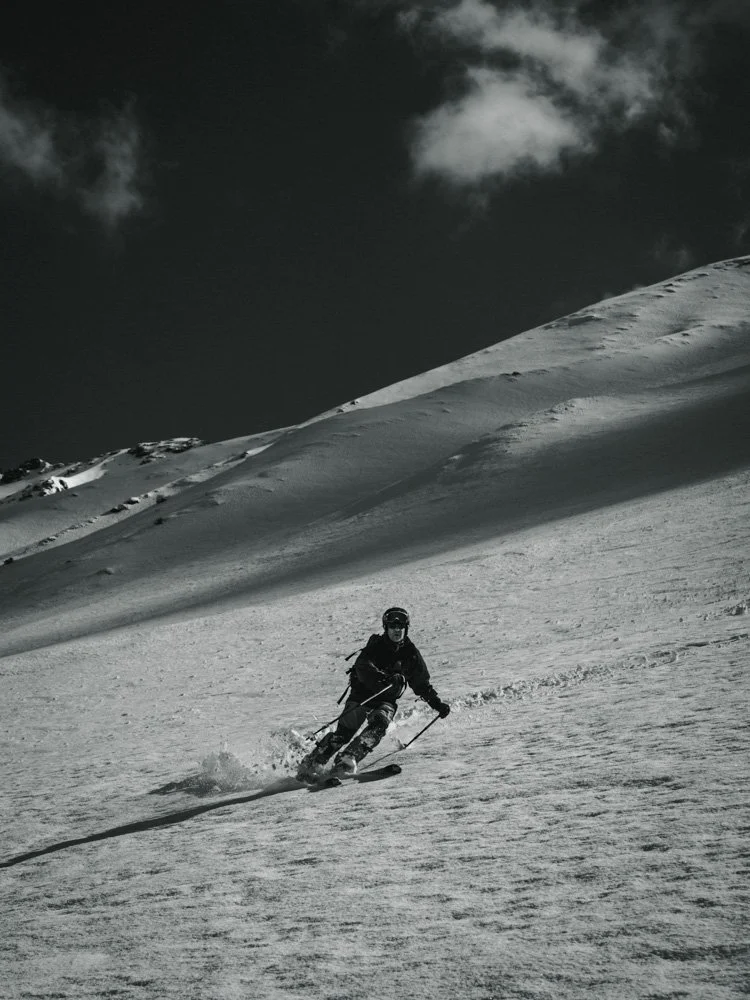 Skifahrer auf schneebedecktem Berg unter dunklem Himmel.