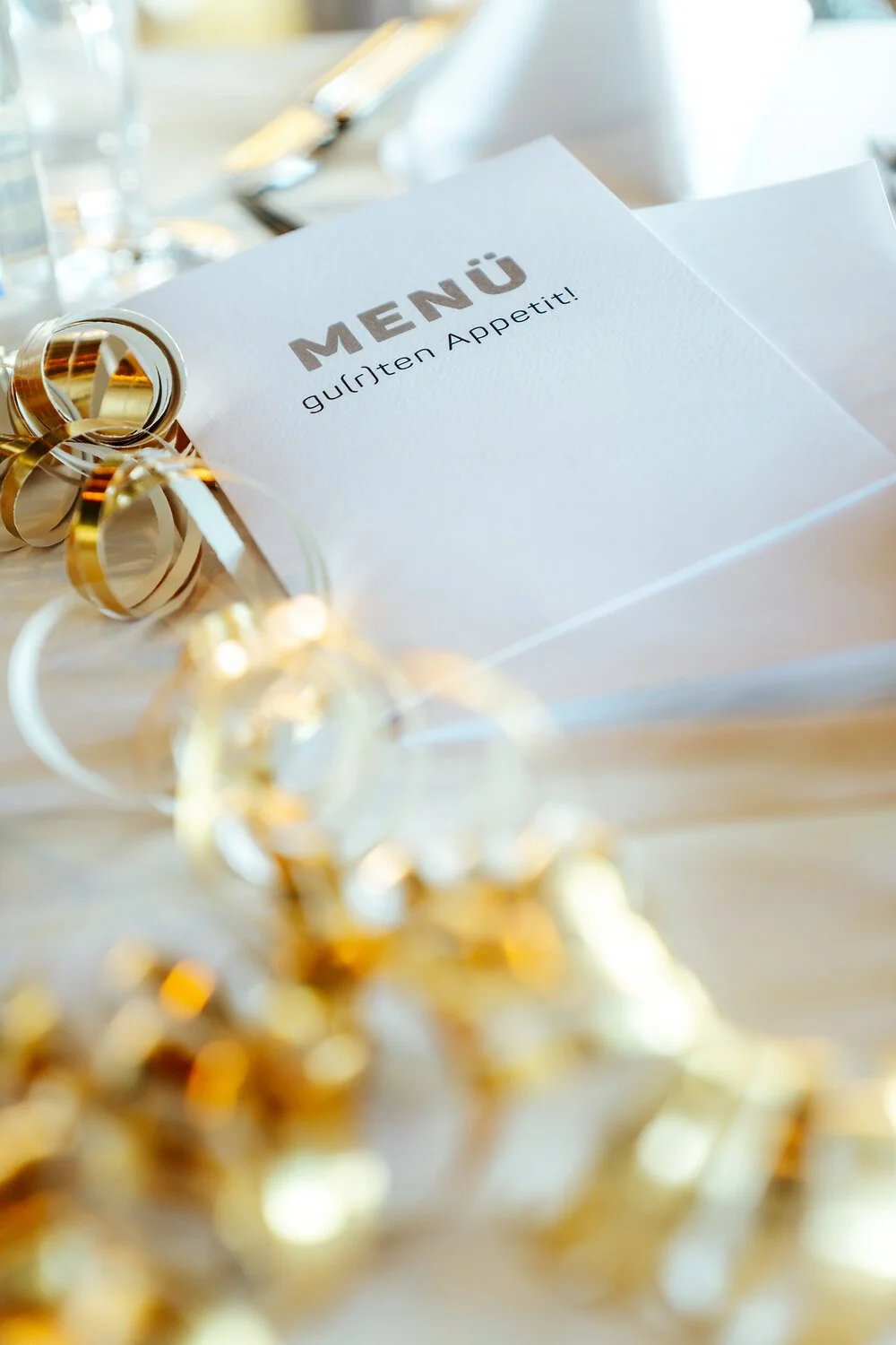 Ein weißes Menü mit goldenen Dekorationen und Konfetti, auf dem steht 'MENÜ' und 'guten Appetit!'.