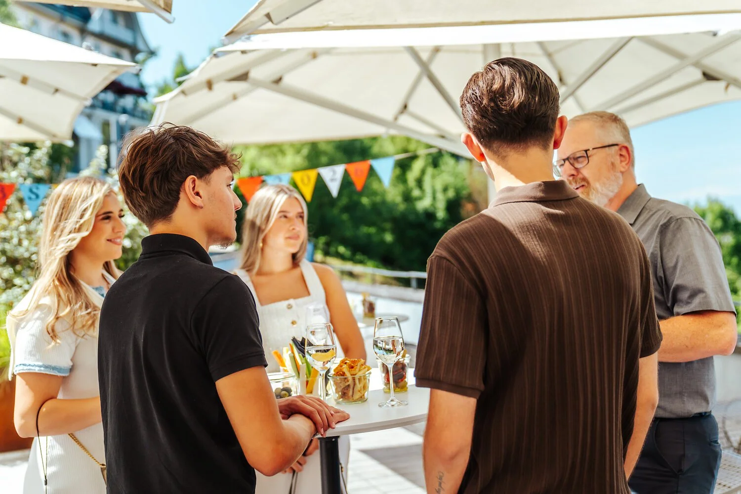 Menschen unter weissen Sonnenschirmen bei einer Feier im Freien, im Hintergrund bunte Fähnchen
