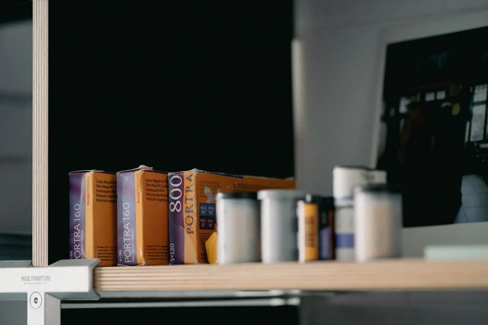 Auf einem Holzregal befinden sich Verpackungen von Fotofilmen und Dosen.