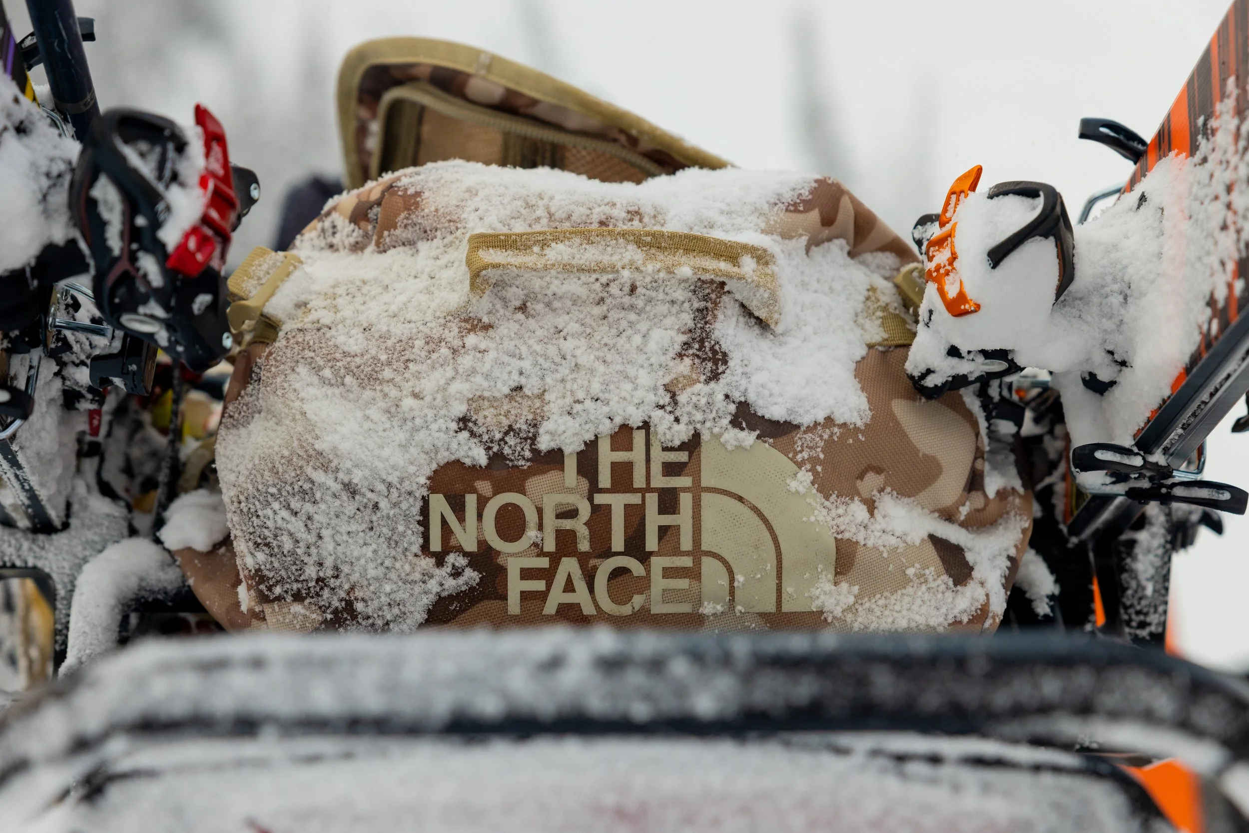 Close-up view of a snowy North Face duffle backpack with snow-covered ski equipment attached.