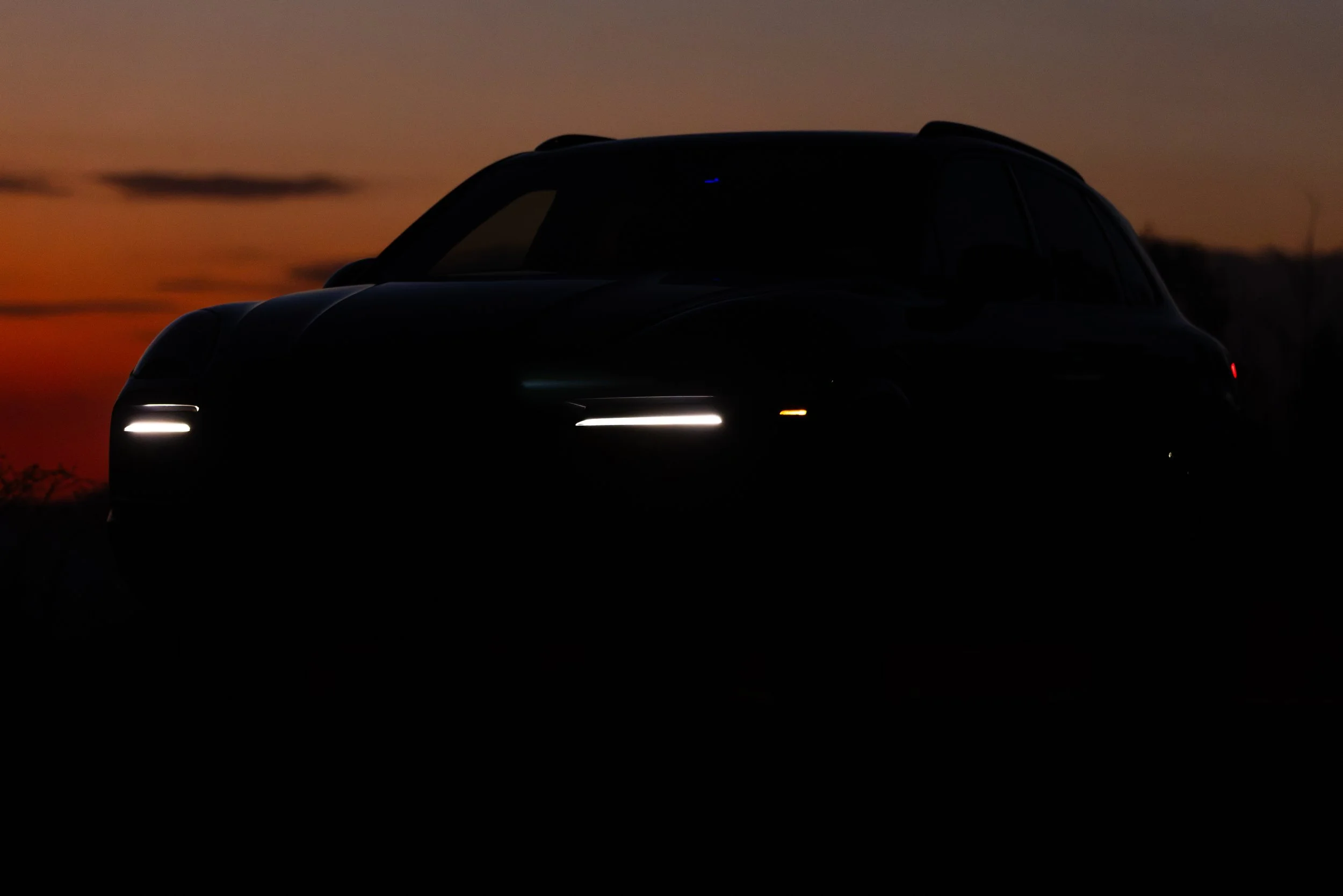 Silhouette of a Porsche Cayenne against a sunset sky with orange and purple hues.