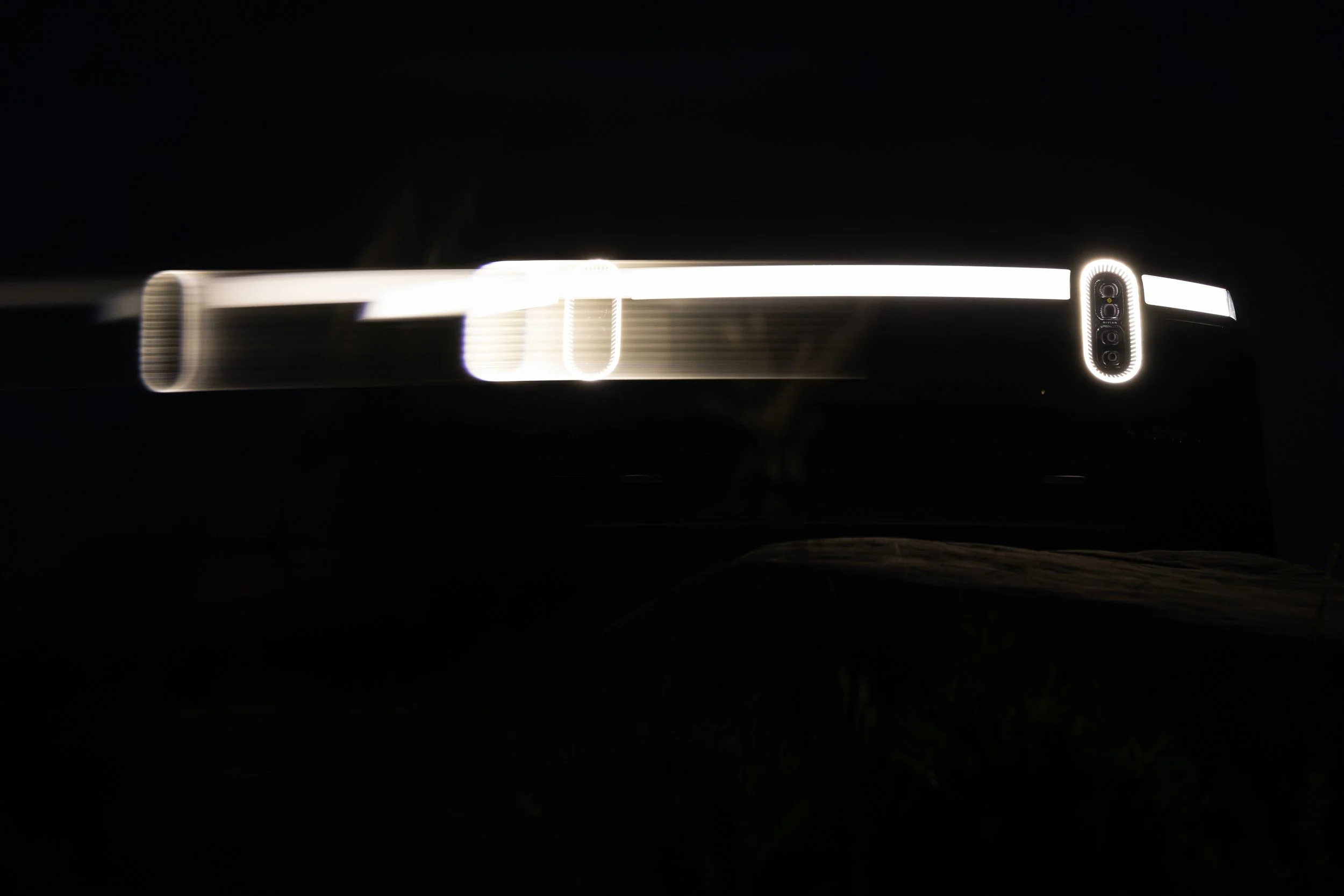 A dark background with a horizontal strip of Rivian R1T lights in the center, and a vertical group of circular lights at the right end.