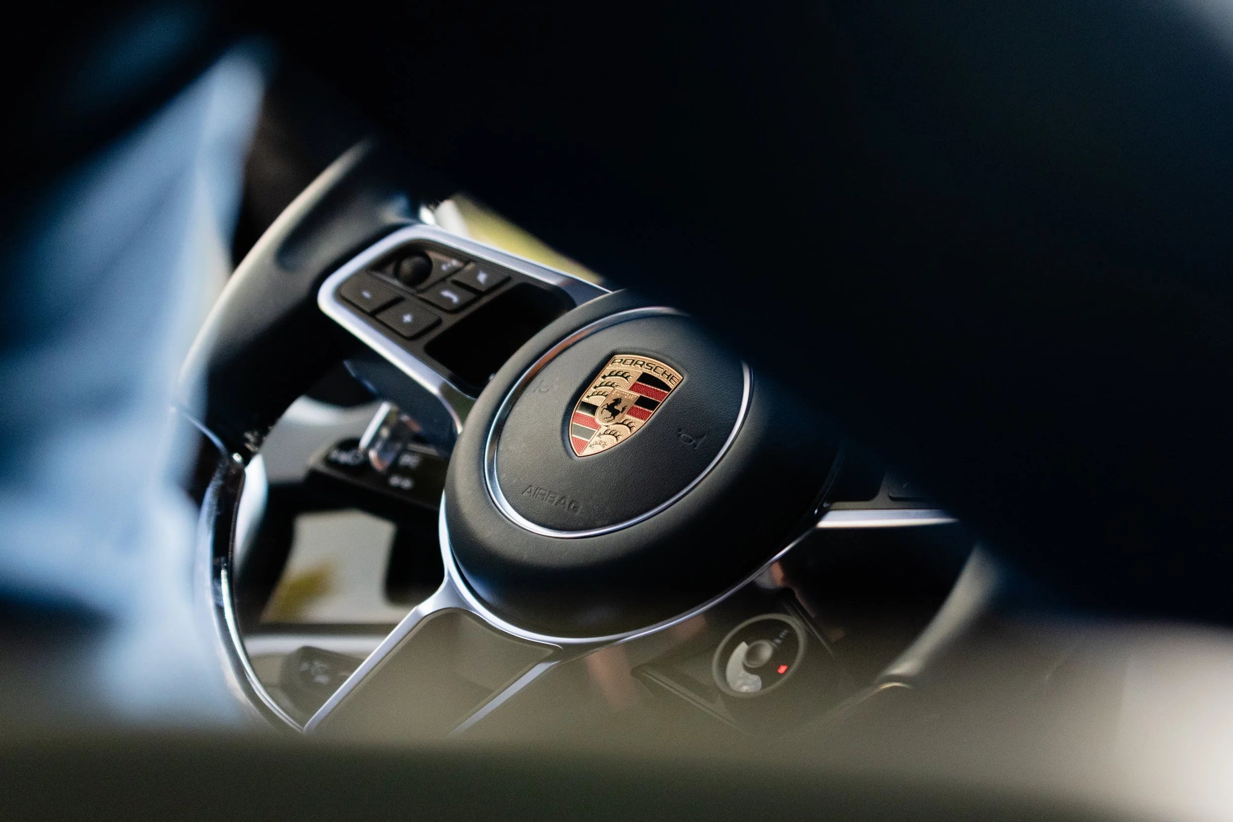 Close-up of Porsche steering wheel with control buttons, partially obscured by dark interior.