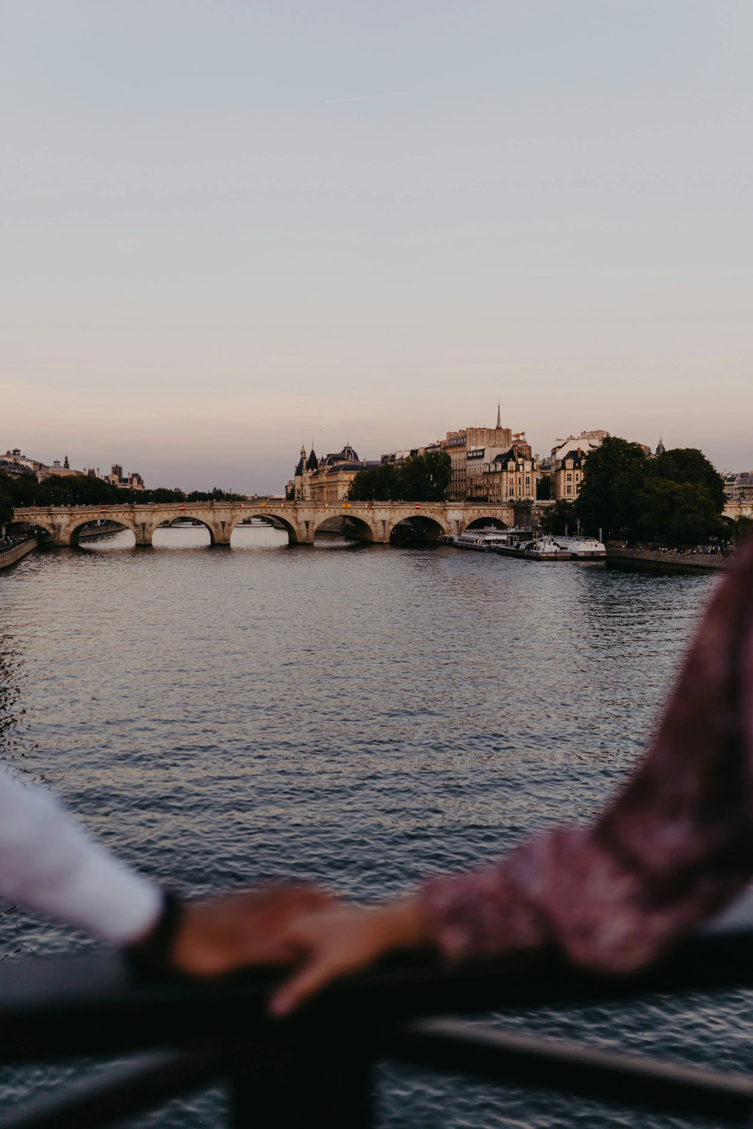 View of the Seine River with historic Parisian buildings and a stone bridge, taken from a boat or along the riverbank during dusk.