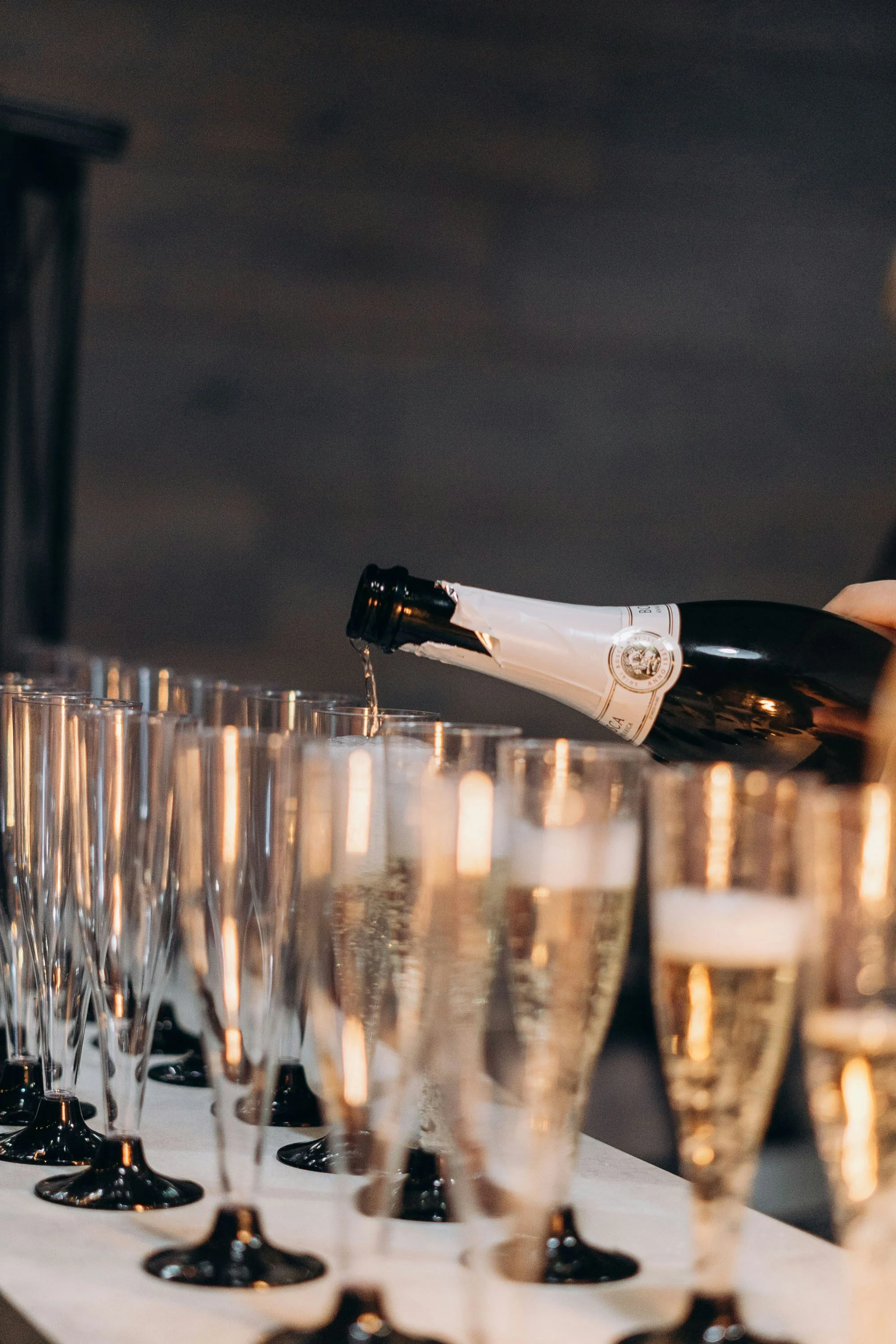A bottle of champagne being poured into clear champagne flutes on a table, with the focus on the glasses and the pouring motion.