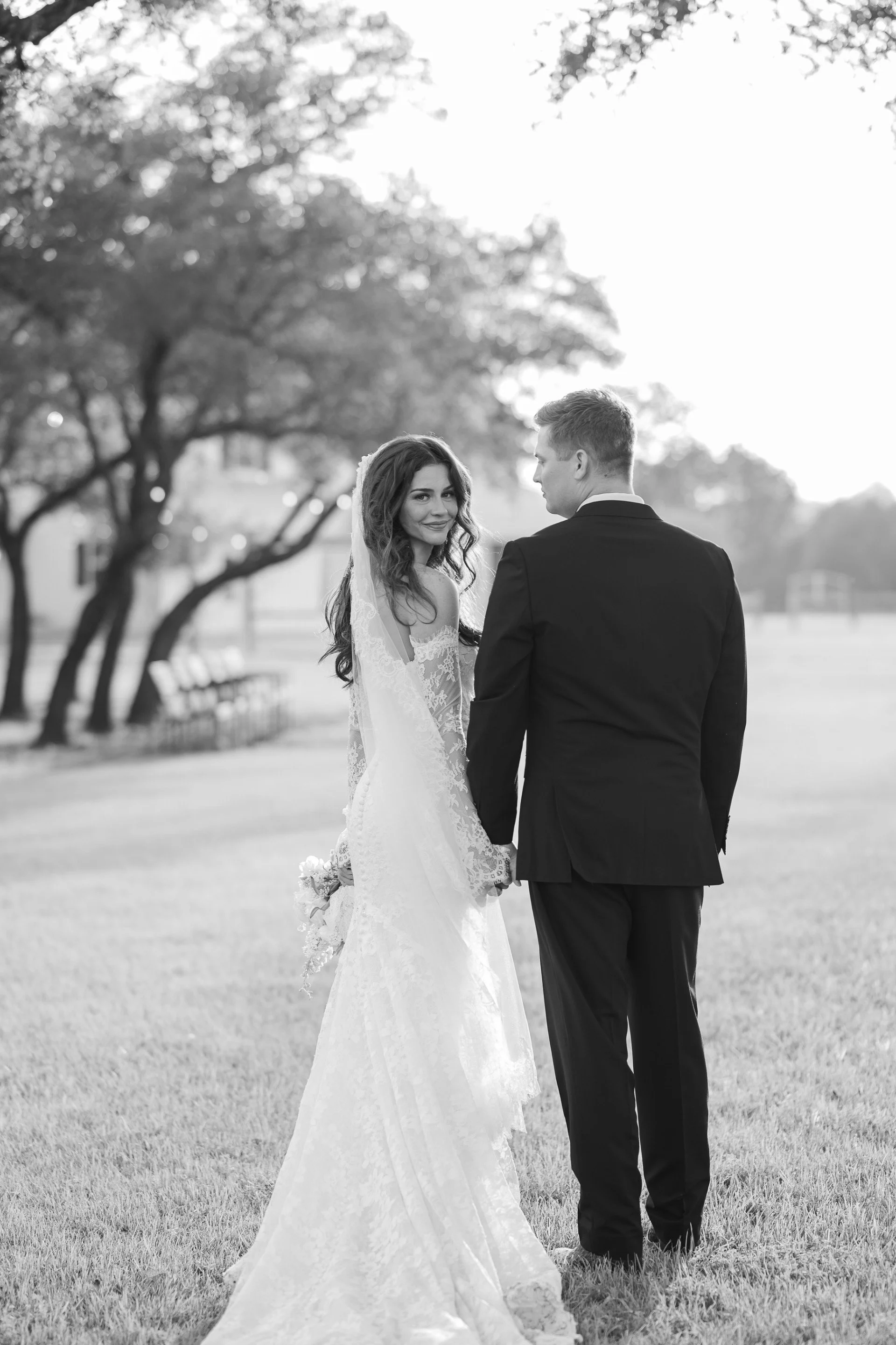 A bride and groom holding hands in a park with trees in the background, black and white photo