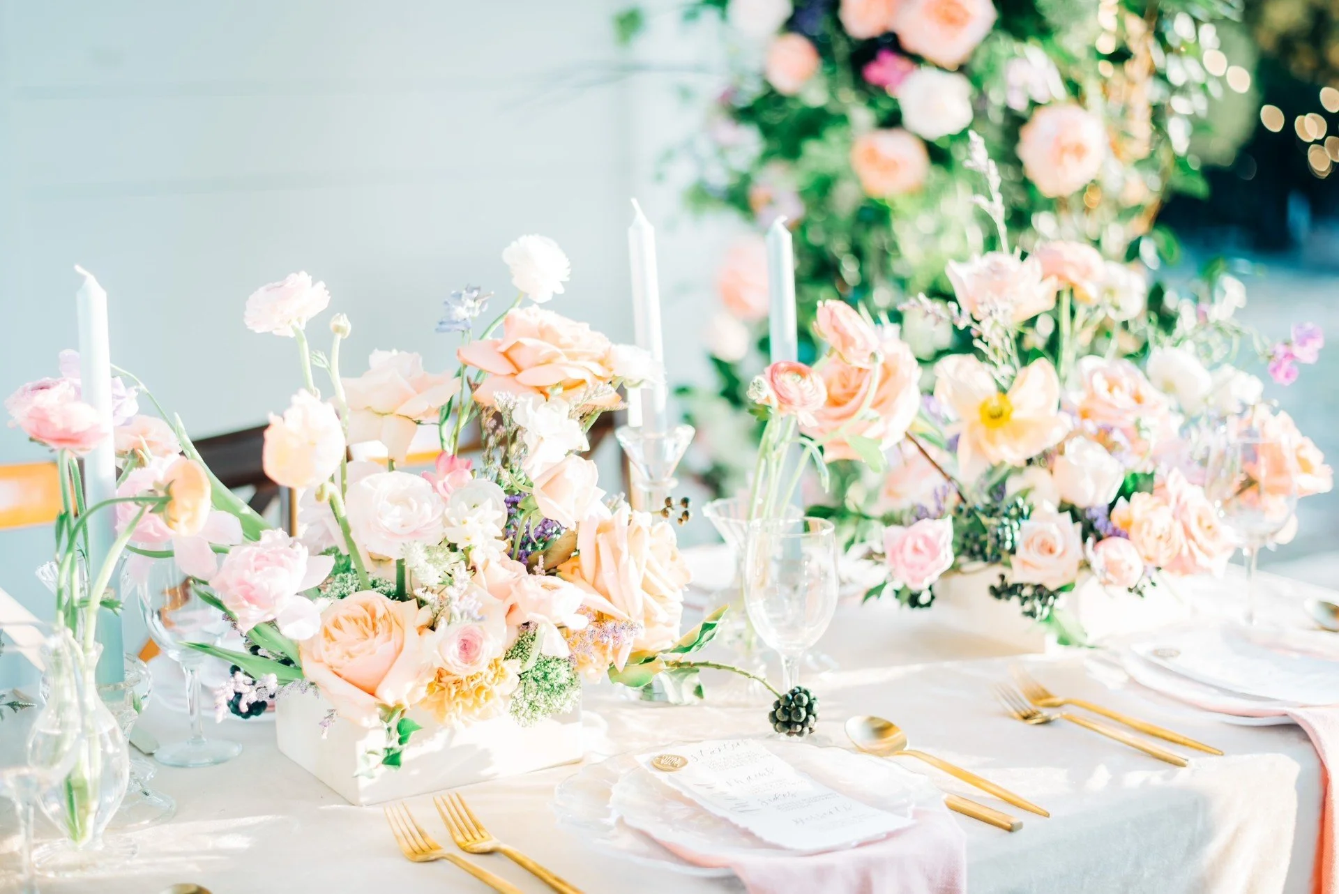 Elegant table setting with floral arrangements, candles, and gold cutlery at a celebration event.