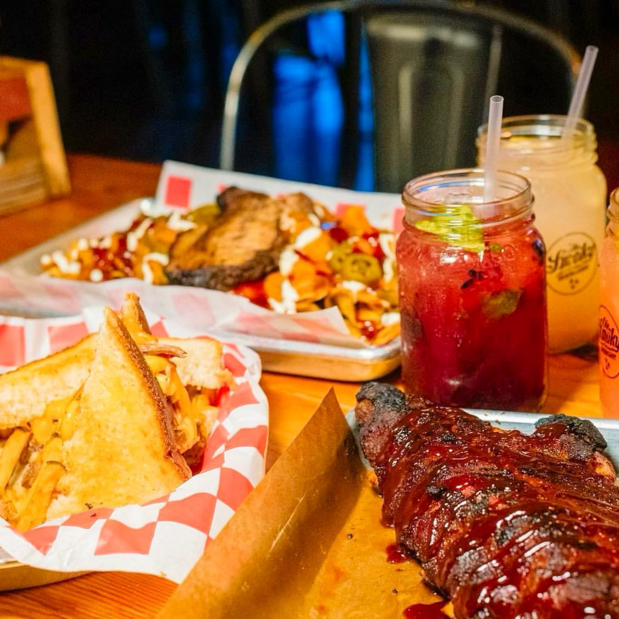Barbecue ribs with barbecue sauce and side of potato chips on a tray, with drinks in jars and straws in the background.