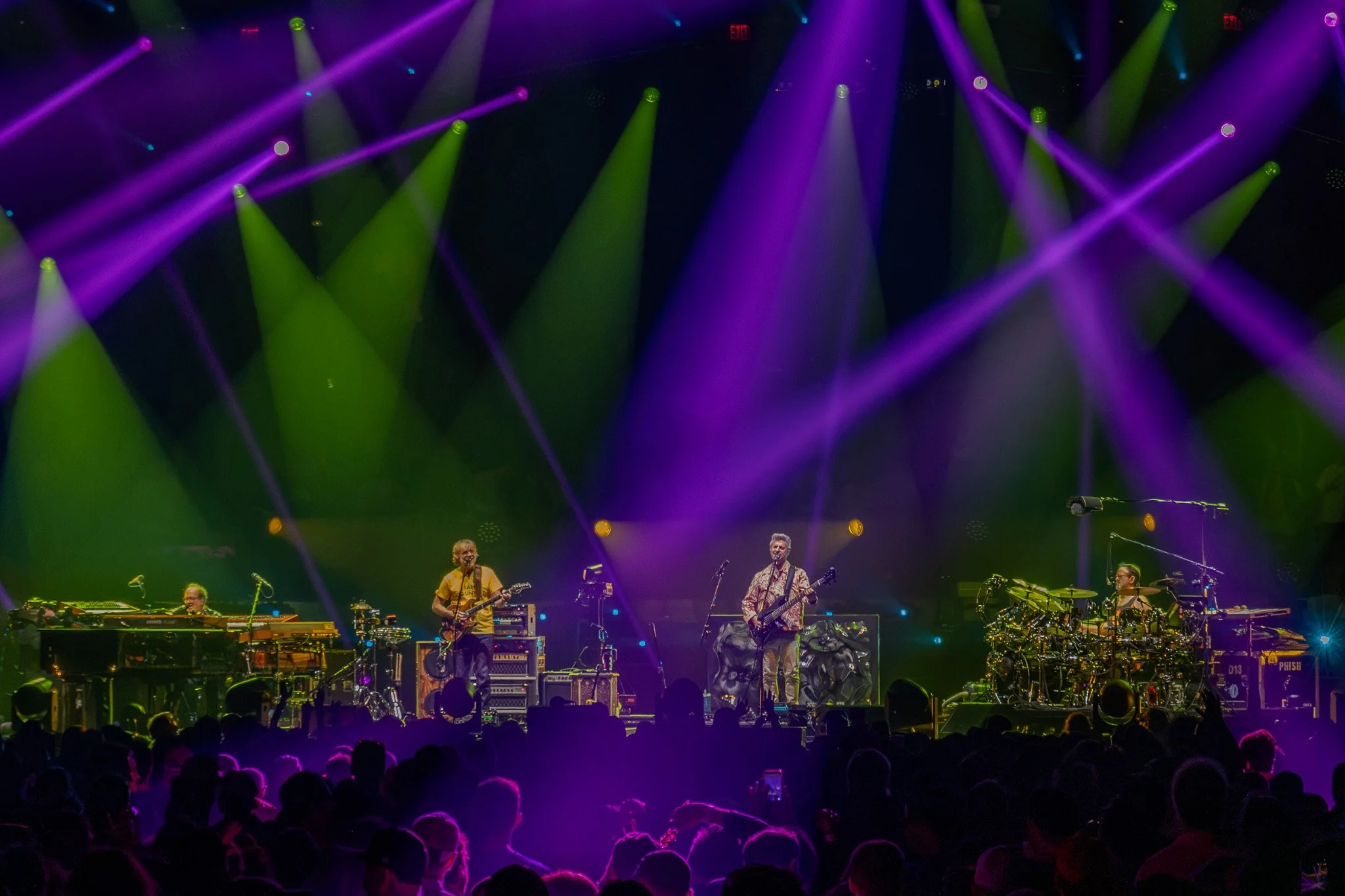 A band performing on stage with colorful purple and green lights, with an audience watching.