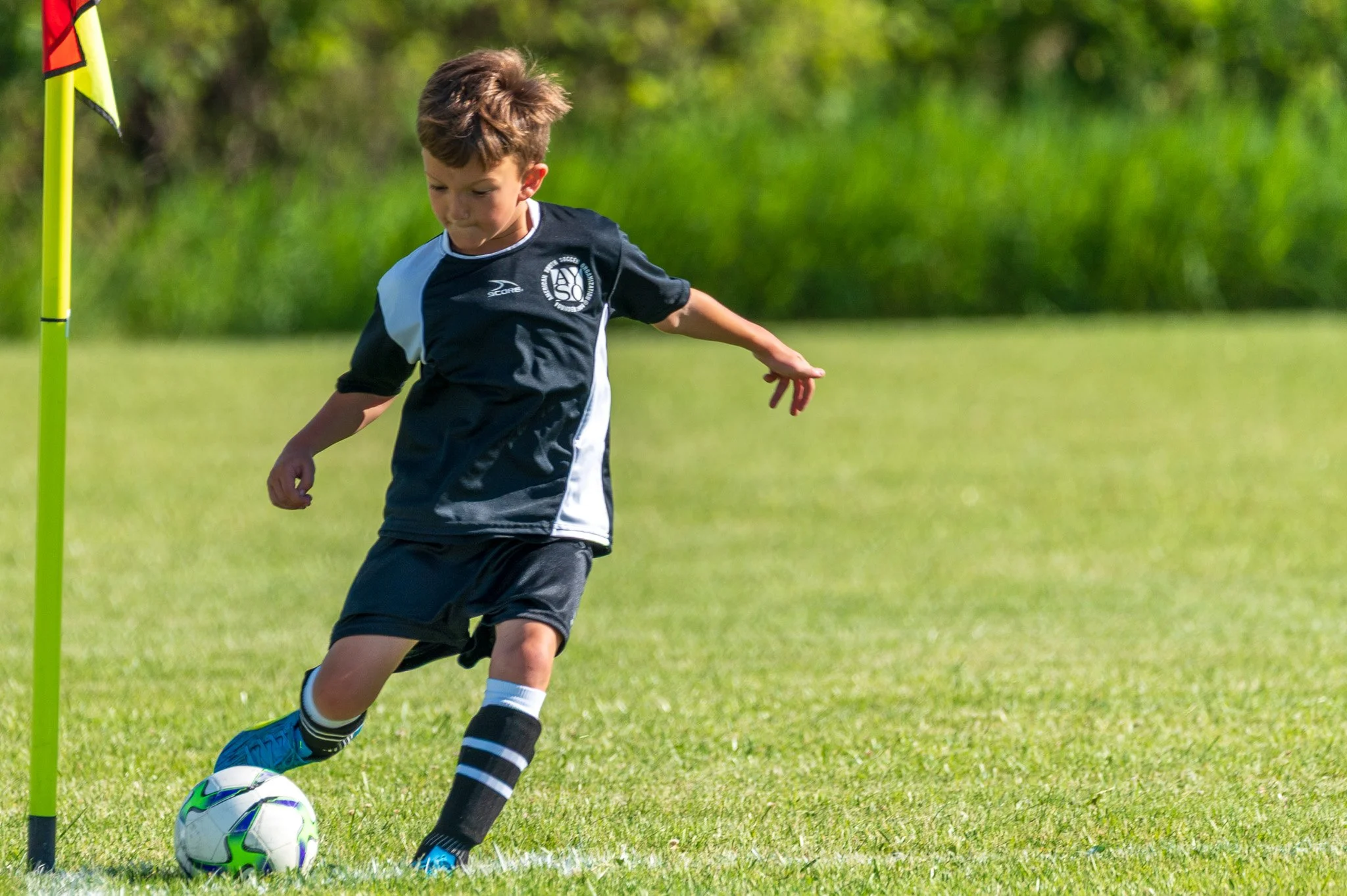 Young boy playing soccer on a grassy field, dribbling the ball past a yellow training pole.