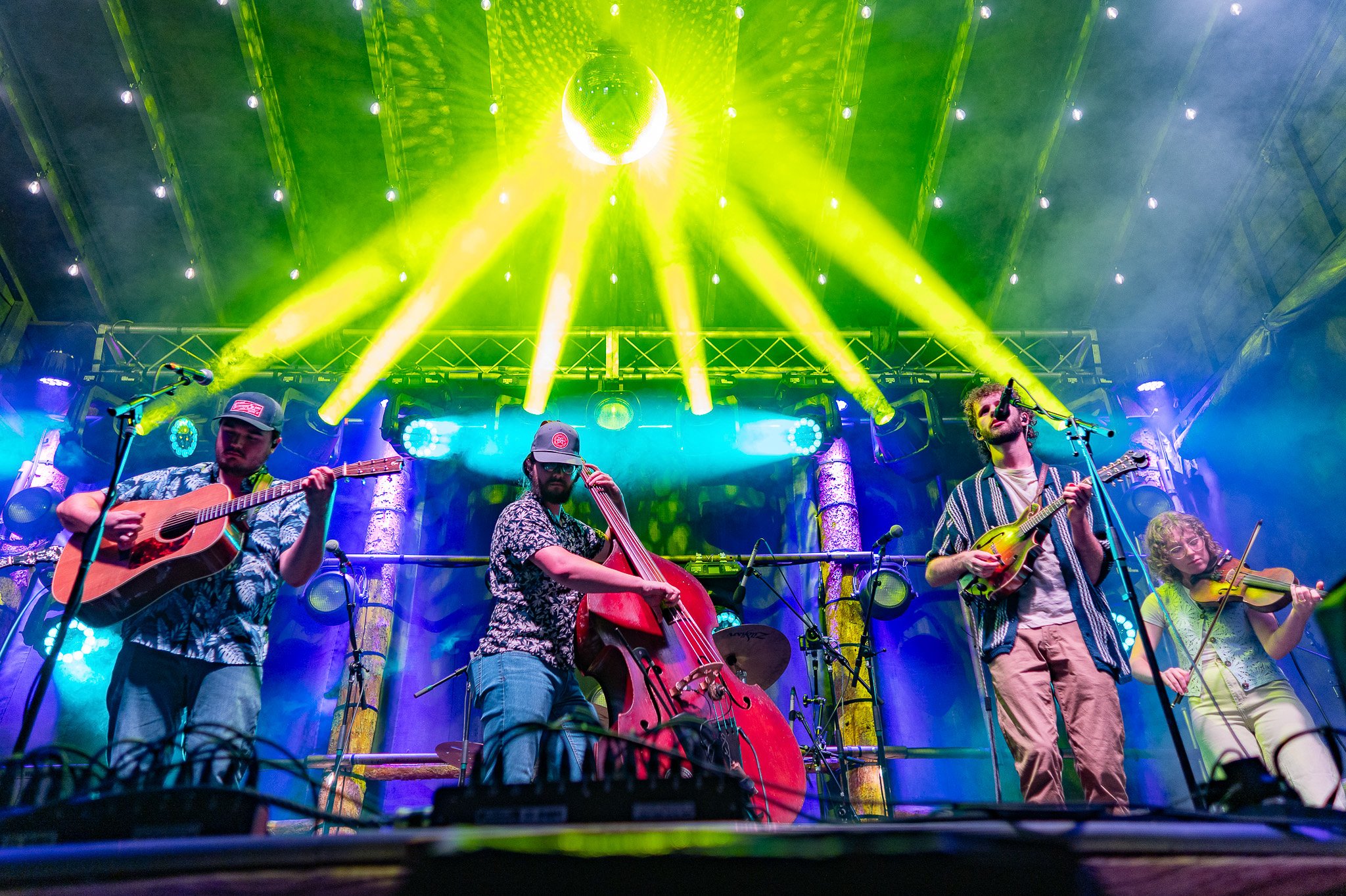 Musicians playing instruments on a stage with colorful lighting and a disco ball overhead.