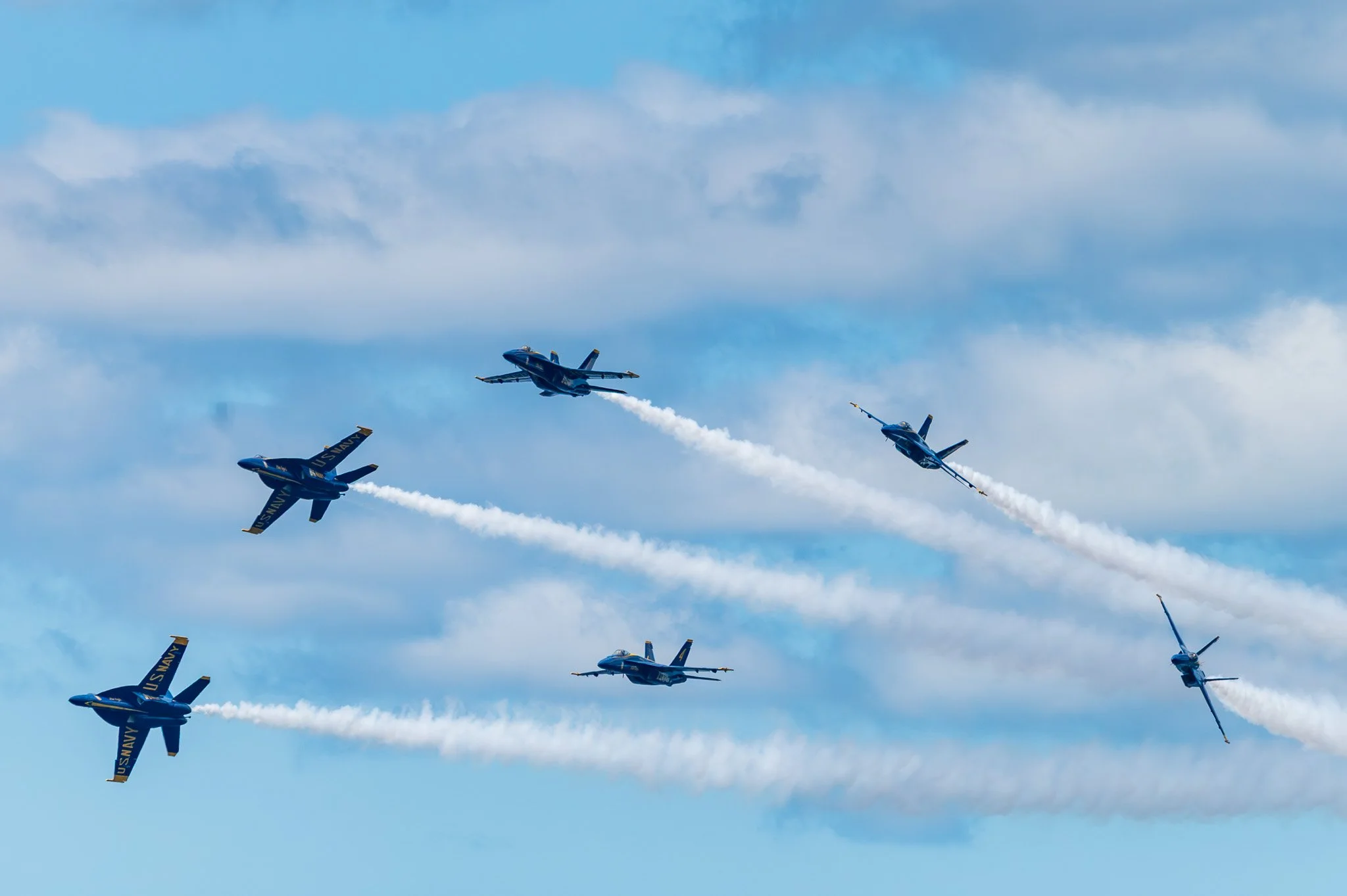 US Navy fighter jets flying in a formation with smoke trails across a cloudy blue sky.