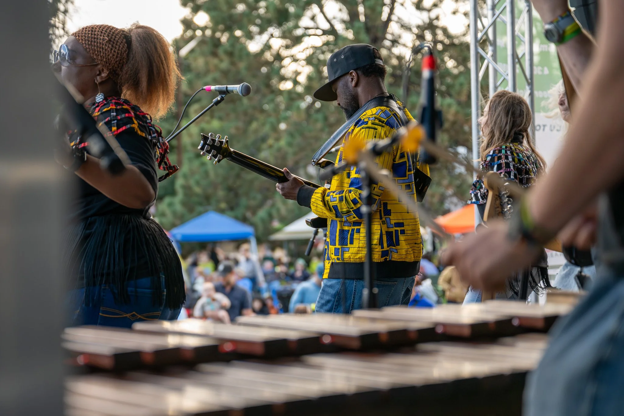 Musicians performing outdoors at a festival, with a woman singing into a microphone and a man playing guitar.