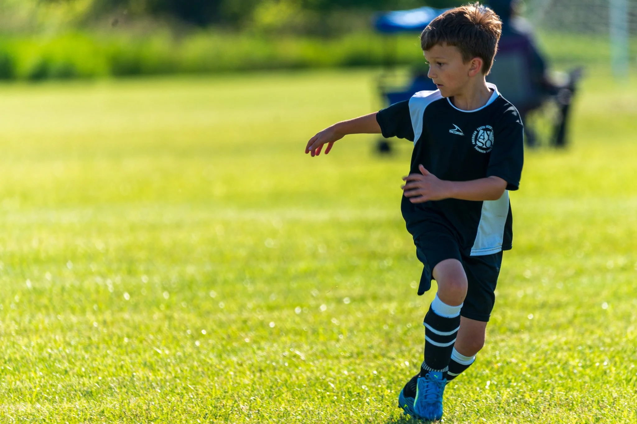 Young boy wearing a black sports uniform running on a grassy field during daytime.