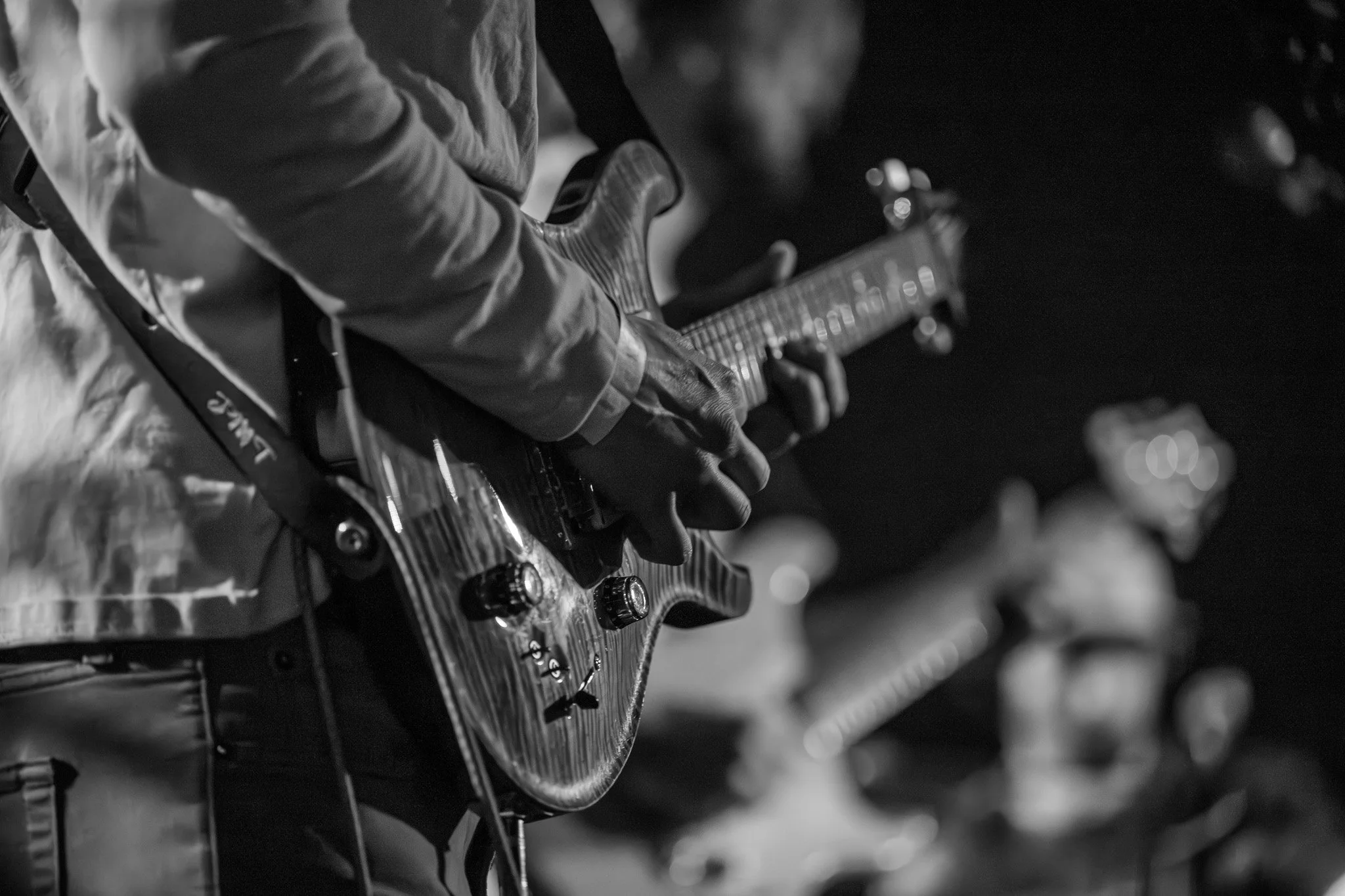 A person playing an electric guitar on a dark stage, captured in black and white.