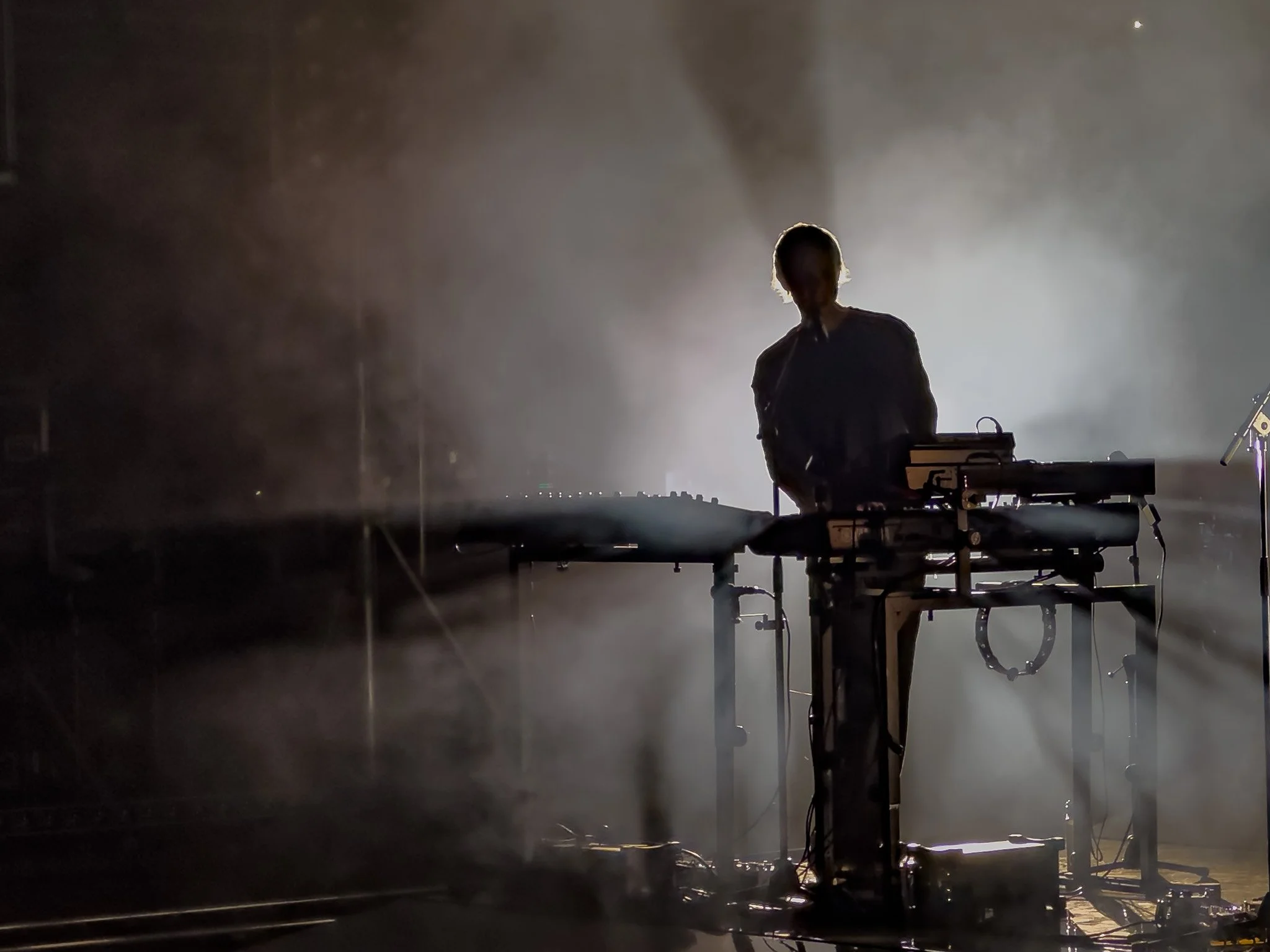 A silhouette of a person standing behind a DJ or music equipment with bright light shining behind them, creating a halo effect around the person's head.